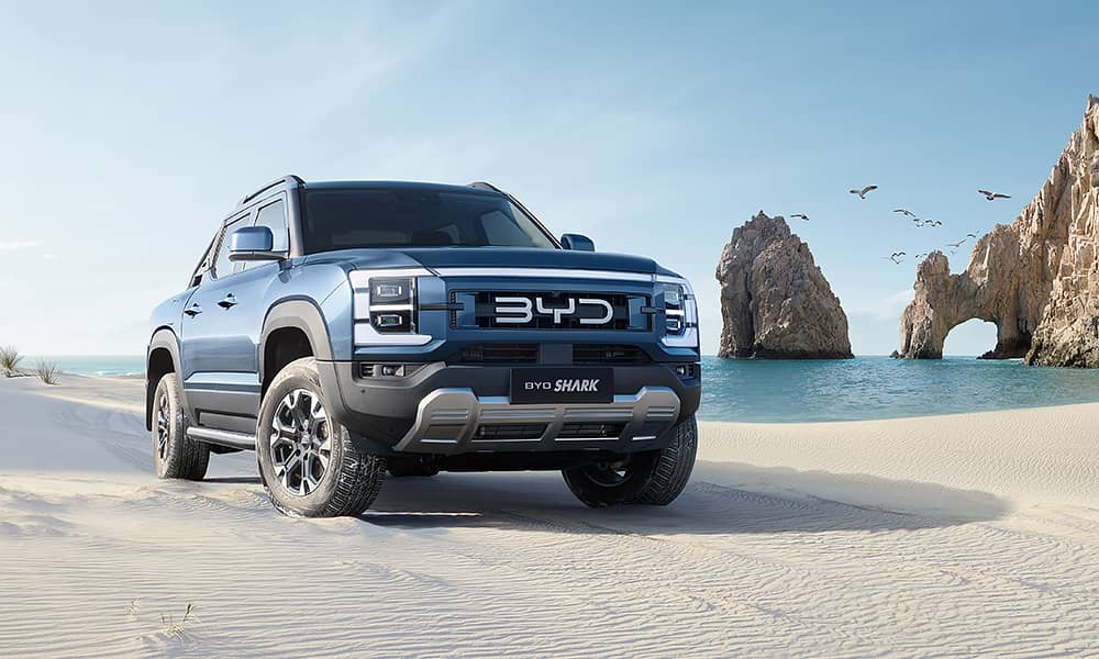 A blue BYD shark ute on a white sand beach