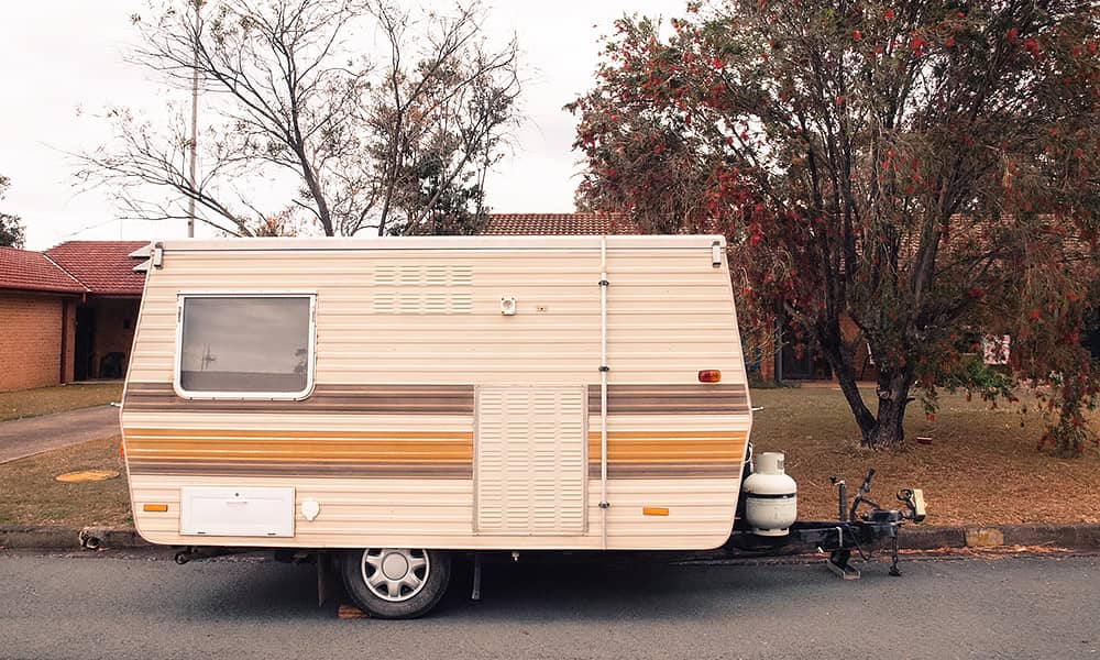 An older style, small caravan parked on the road outside a house