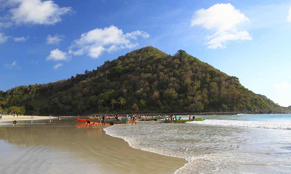 A tropical beach with boats on shore and a hill in the distance