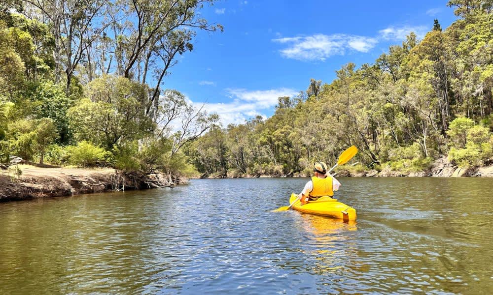 Person paddling down river in yellow kayak