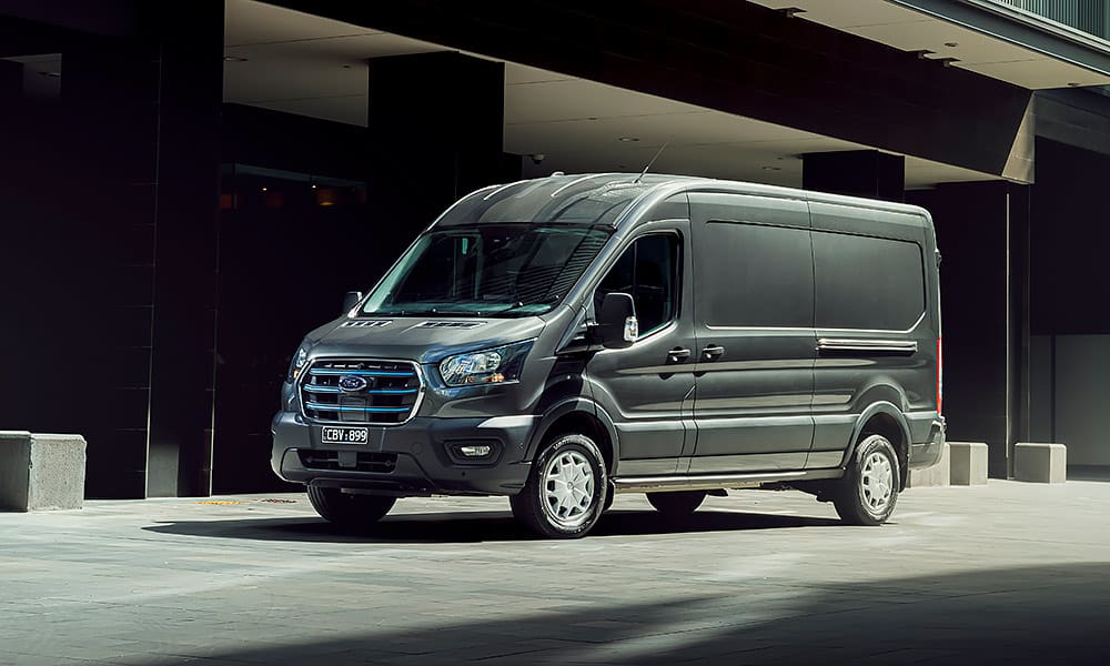 A grey Ford e-Transit van parked outside a city building