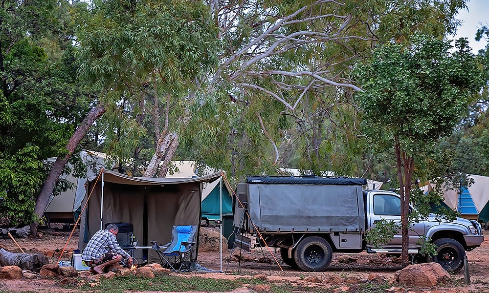 A man tending a campfire near an awning in a caravan park