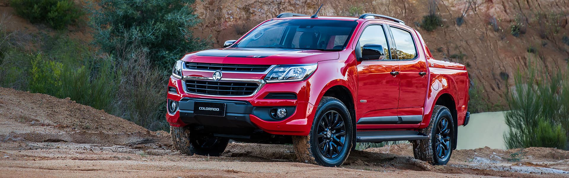 A red Holden Colorado parked near a rock wall.