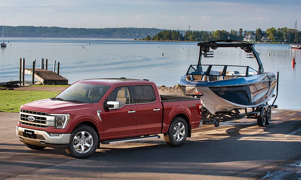 A red Ford F-150 towing a boat from a boat ramp