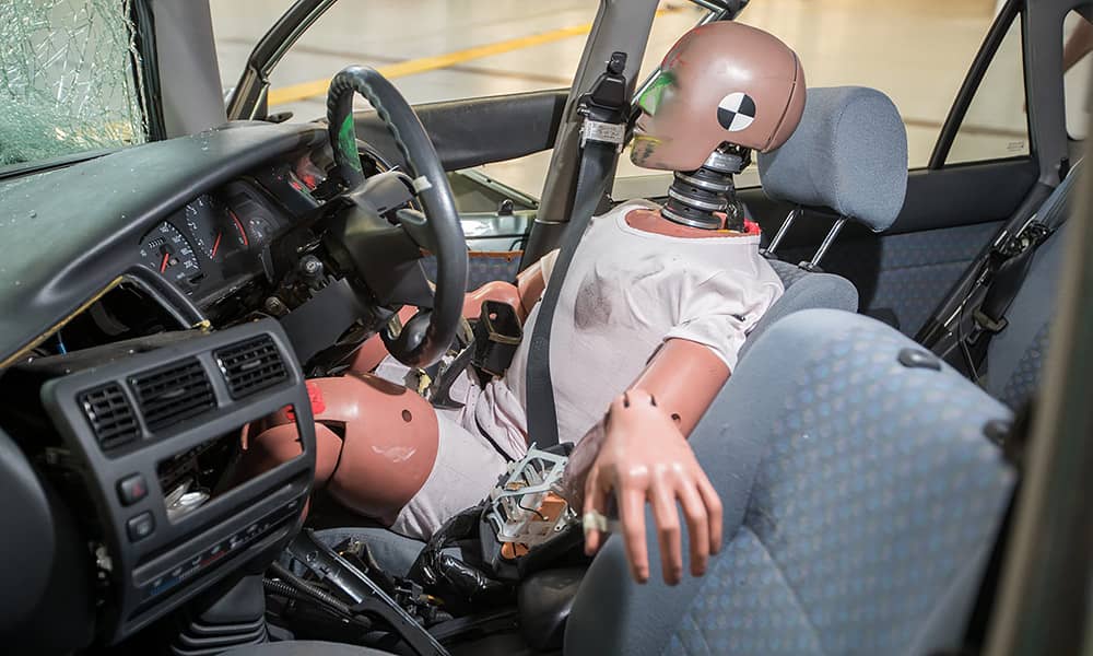 A crash test dummy in the driver's seat of a crashed car