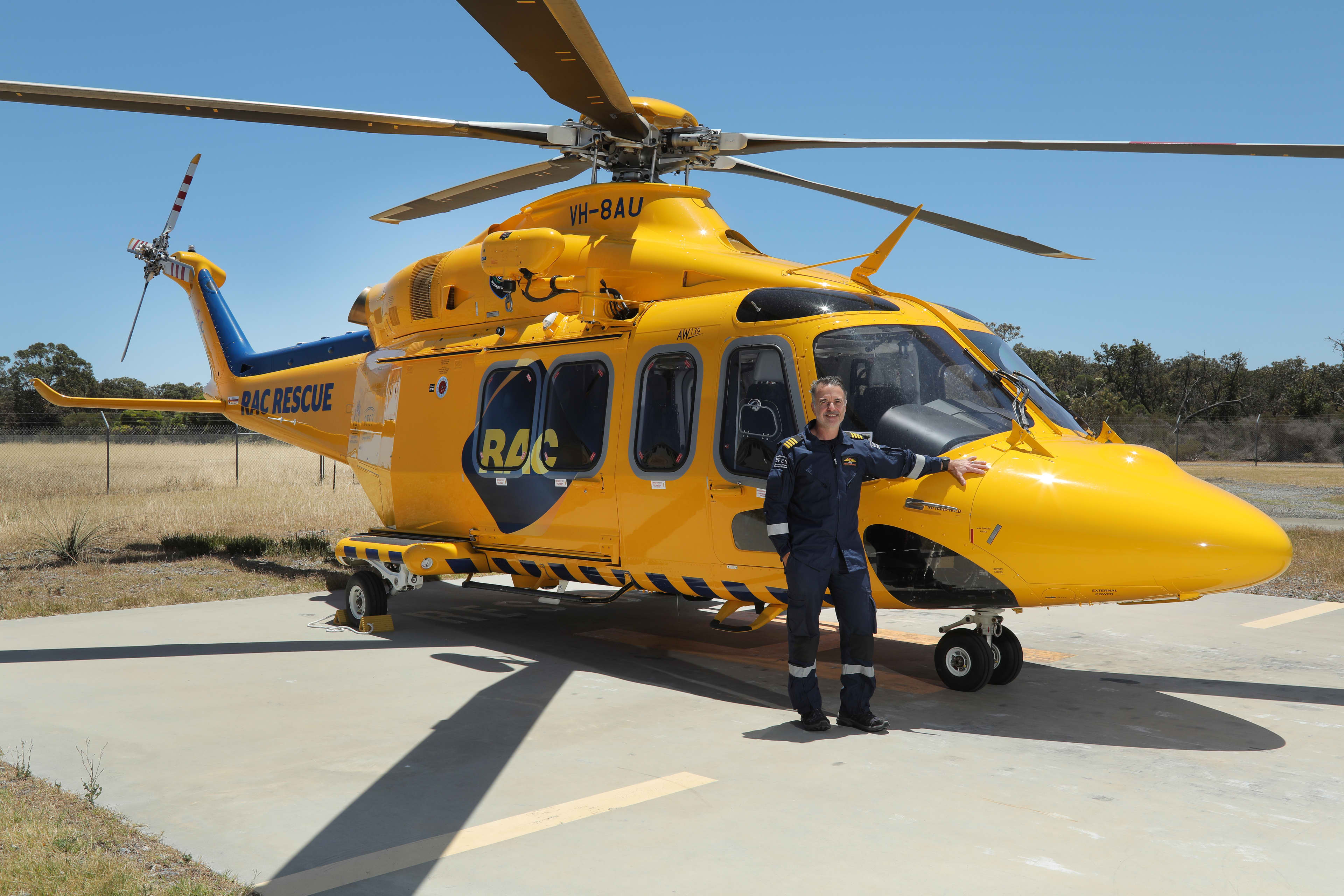 Pilot standing in front of a yellow helicopter on a tarmac.