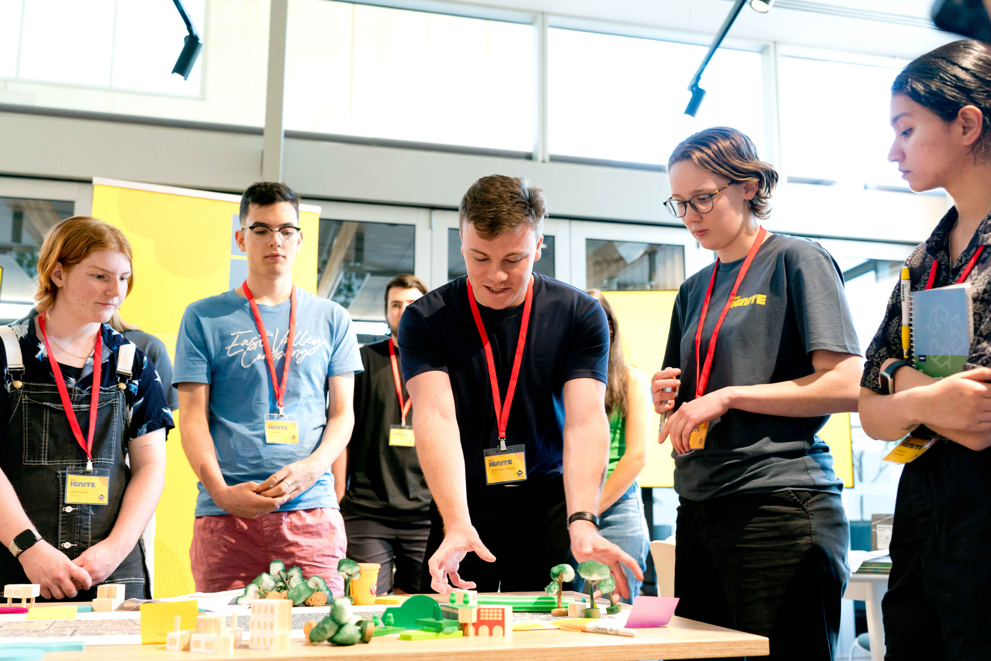 Group of teenagers standing around a table discussing a workshop idea.