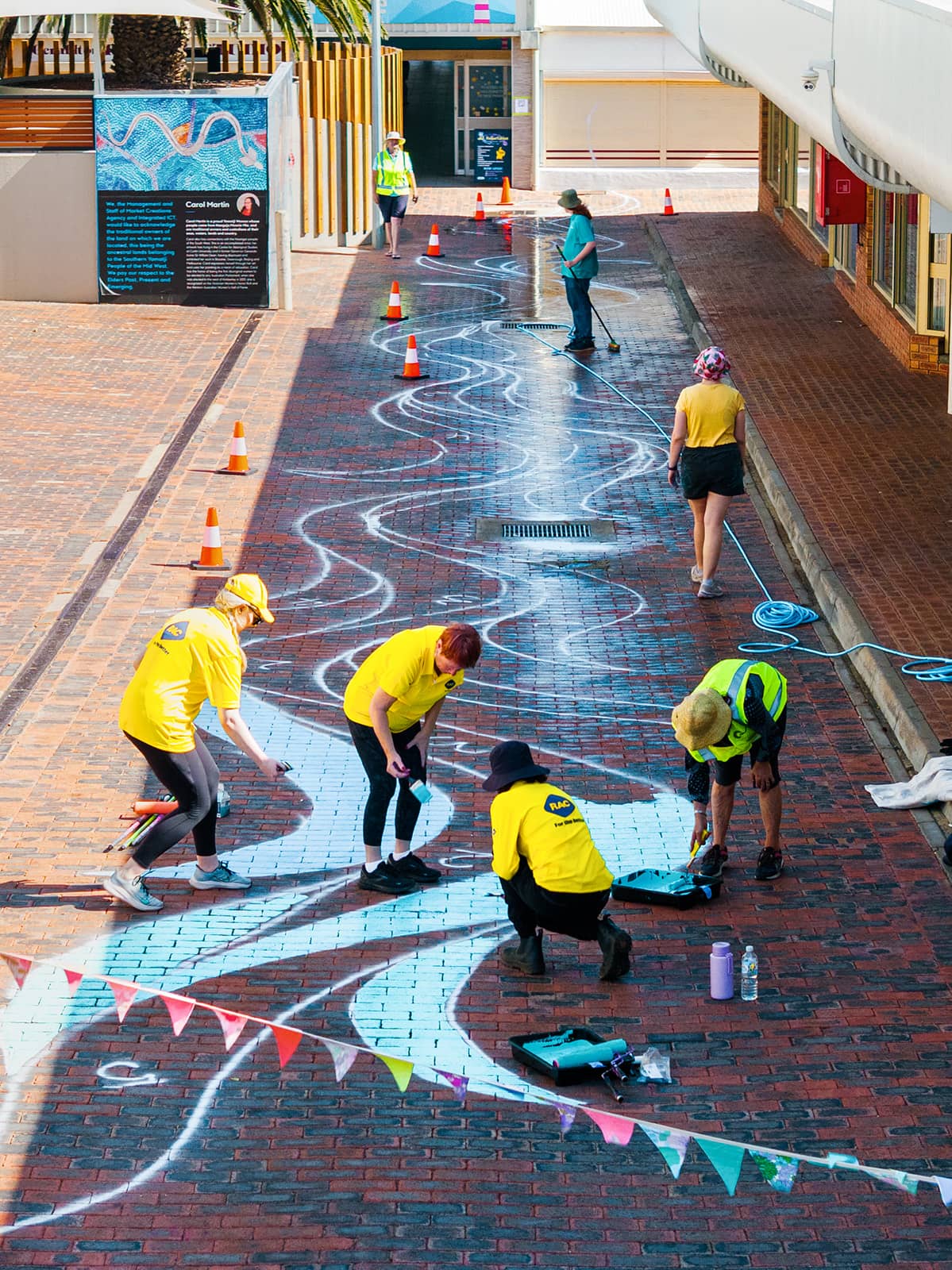 Group of people wearing yellow shirts painting a mural on a street.
