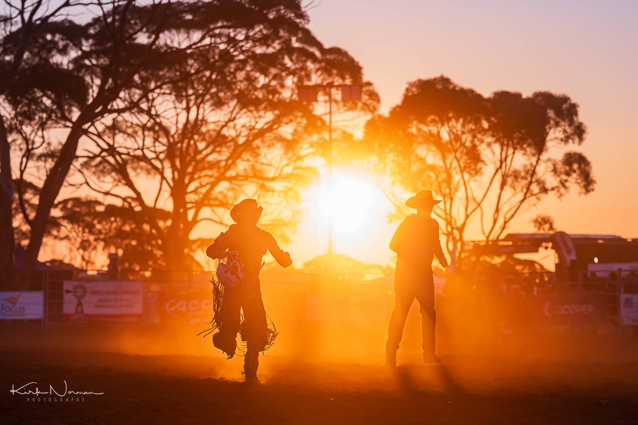 Two people dressed as 'cowboys' silhouetted against the sunset in a paddock