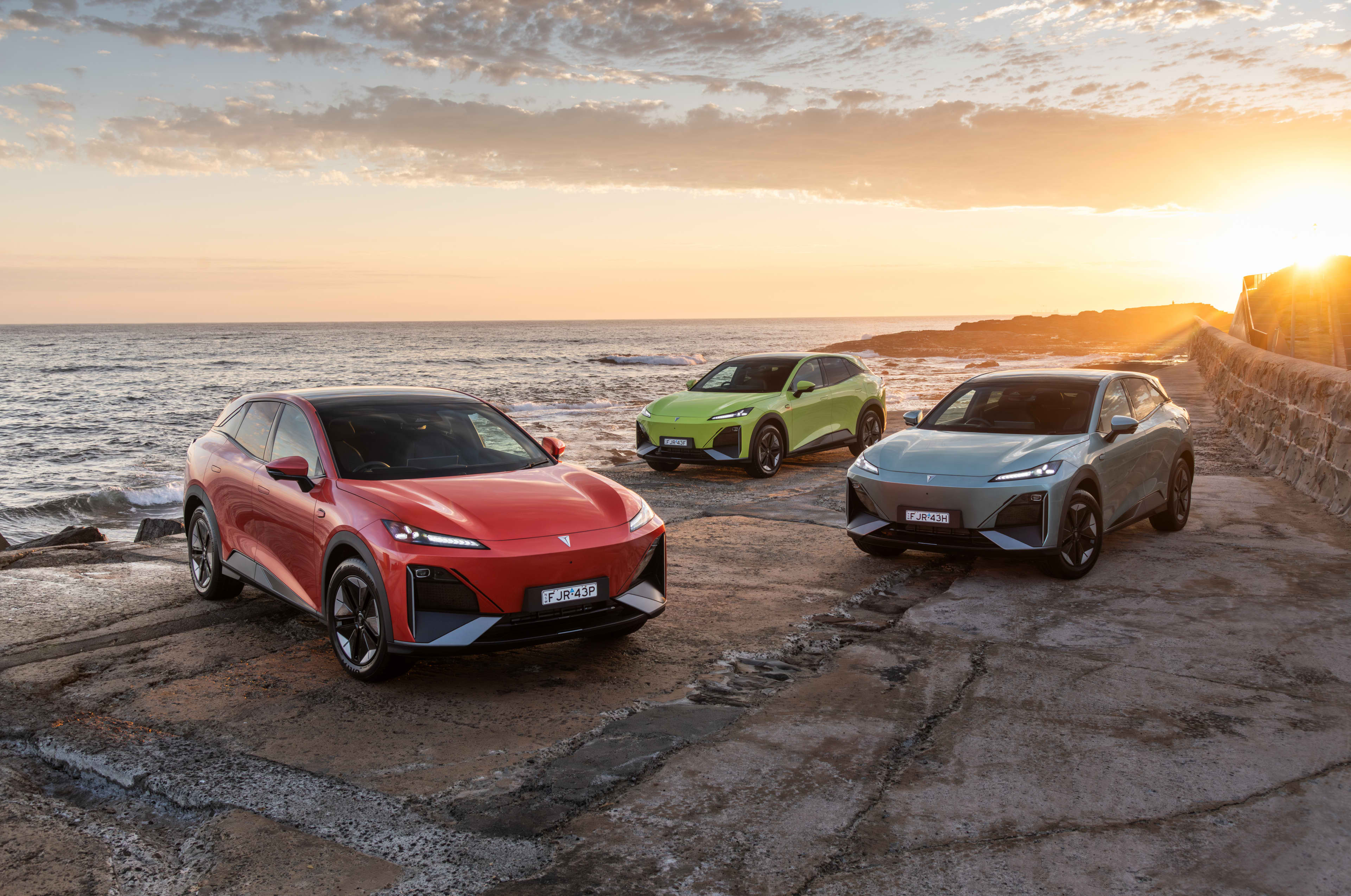 Three Deepal electric vehicles parked in front of a beach at sunset