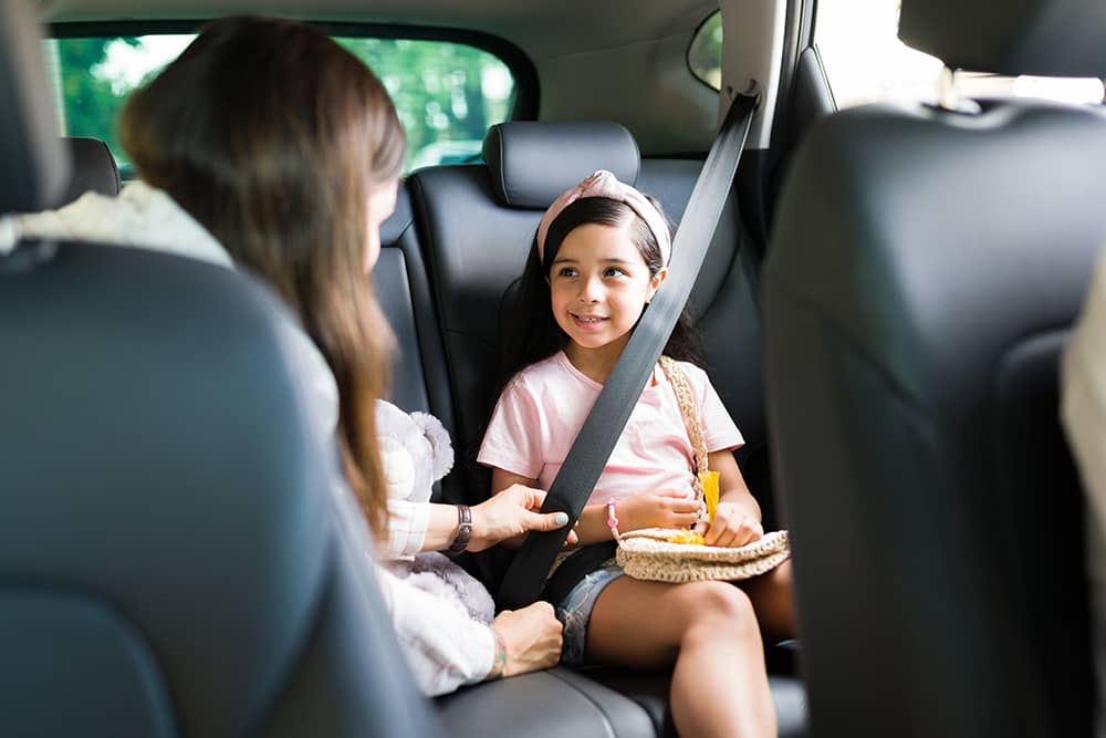 A mother is securing her child in a seatbelt in the rear seat of a car