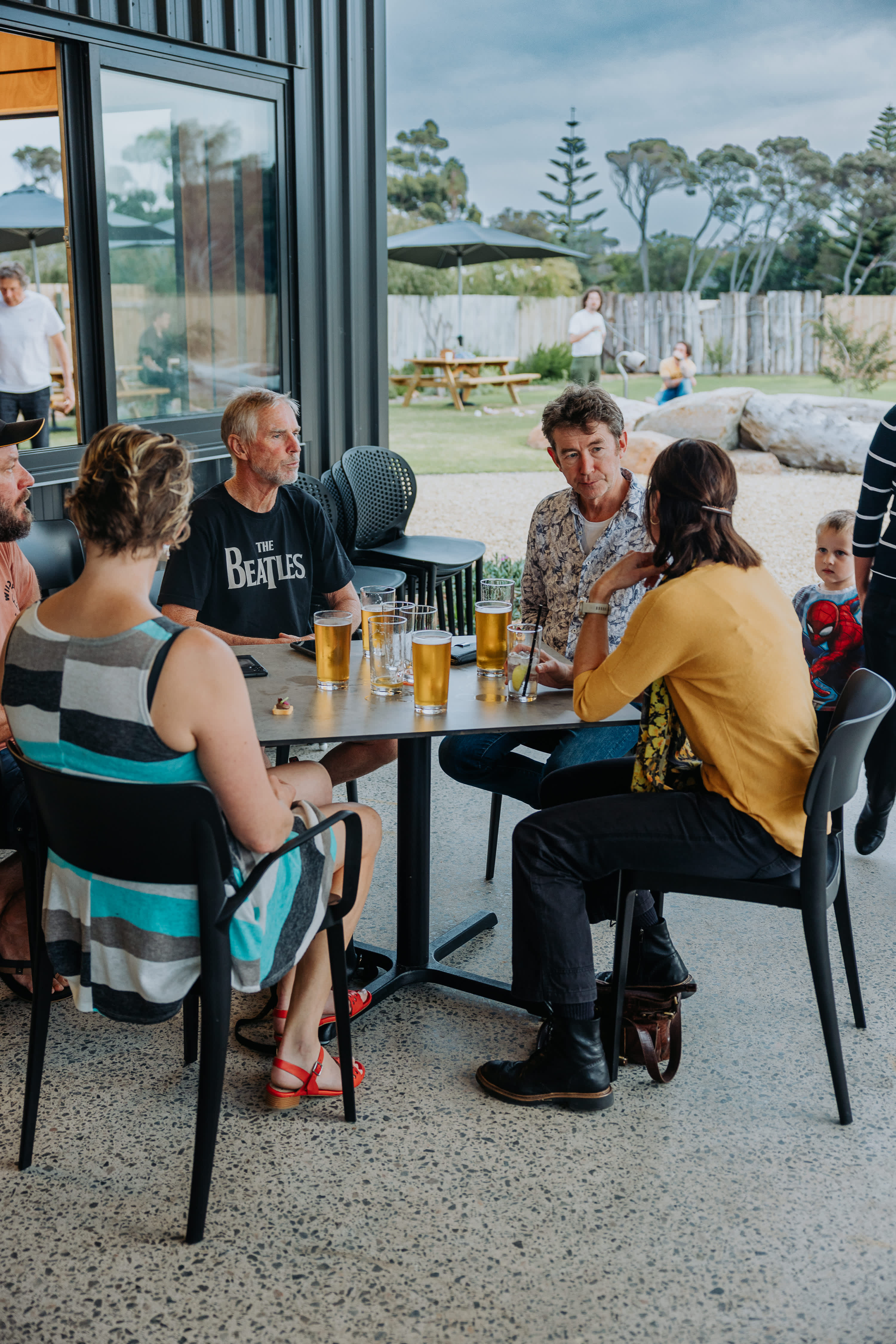 A group of people sitting around Dune Beer Co outside with a playground in the background