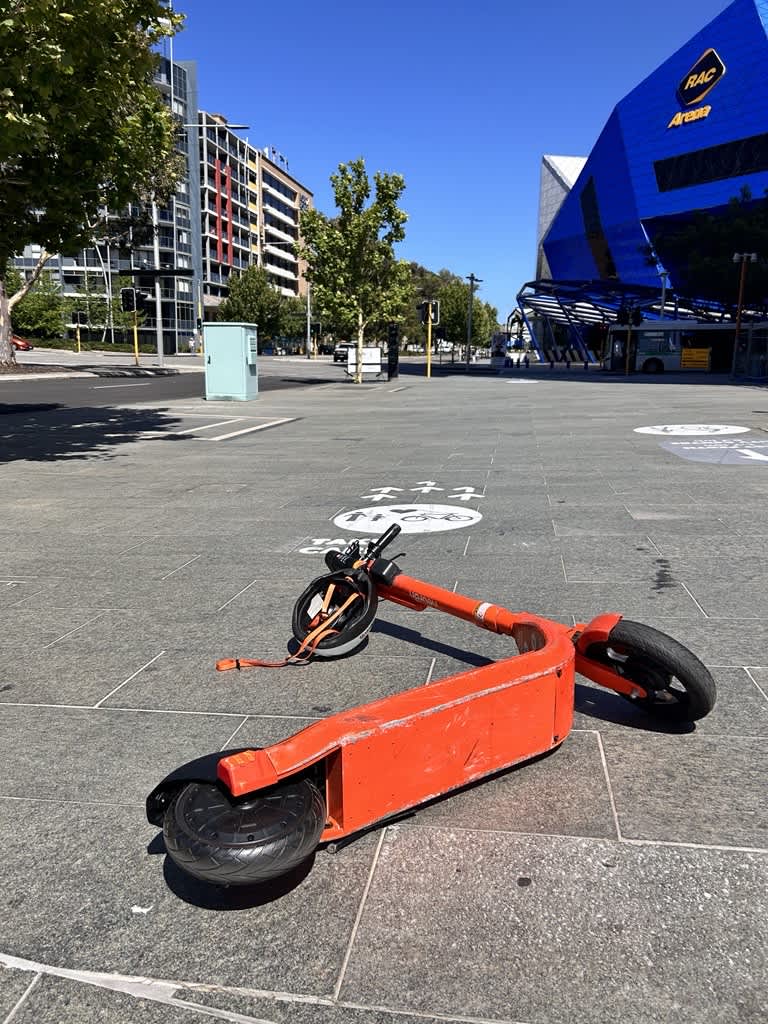 An orange hire scooter abandoned on the footpath outside along a city street