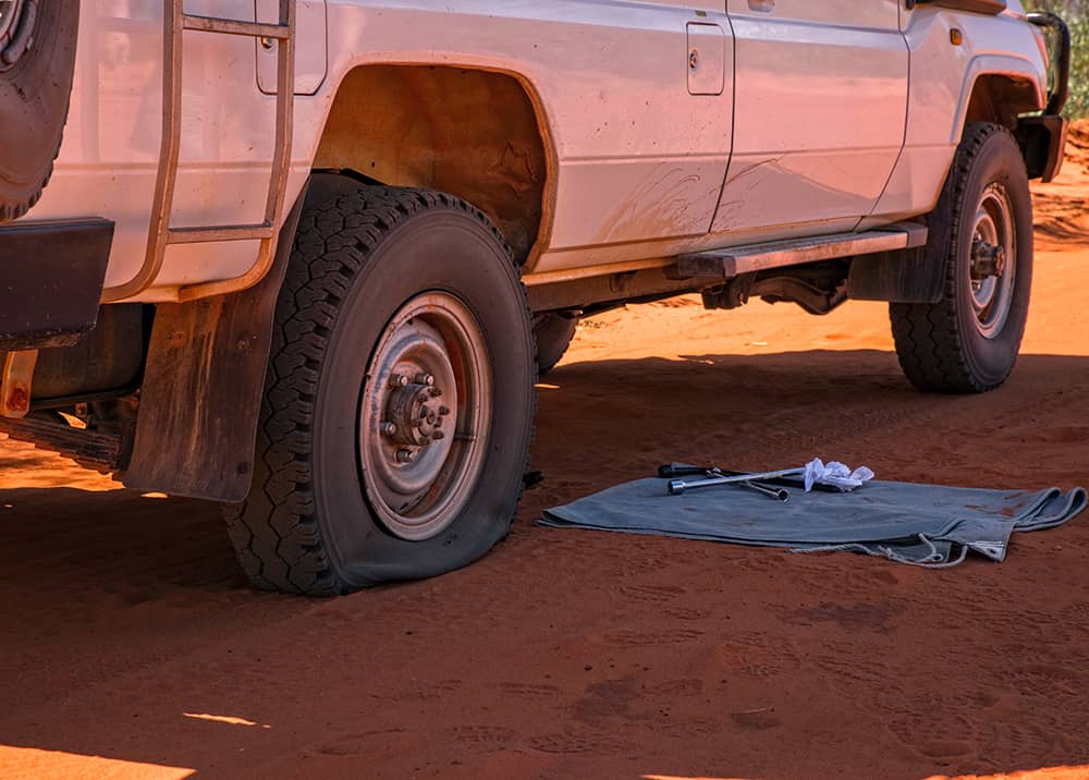 A four-wheel drive vehicle with a flat tyre on a red dirt track