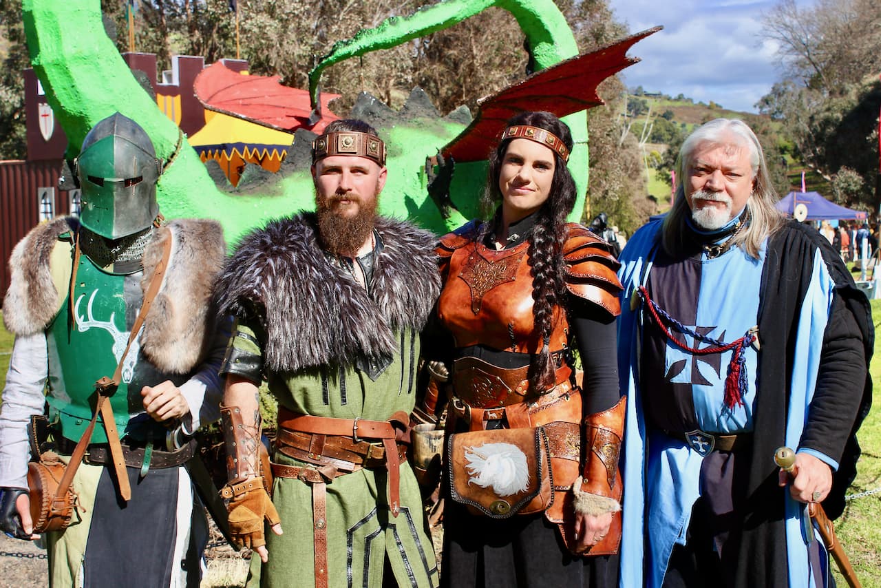 Four people standing together dressed in medieval costumes in front of a paper dragon