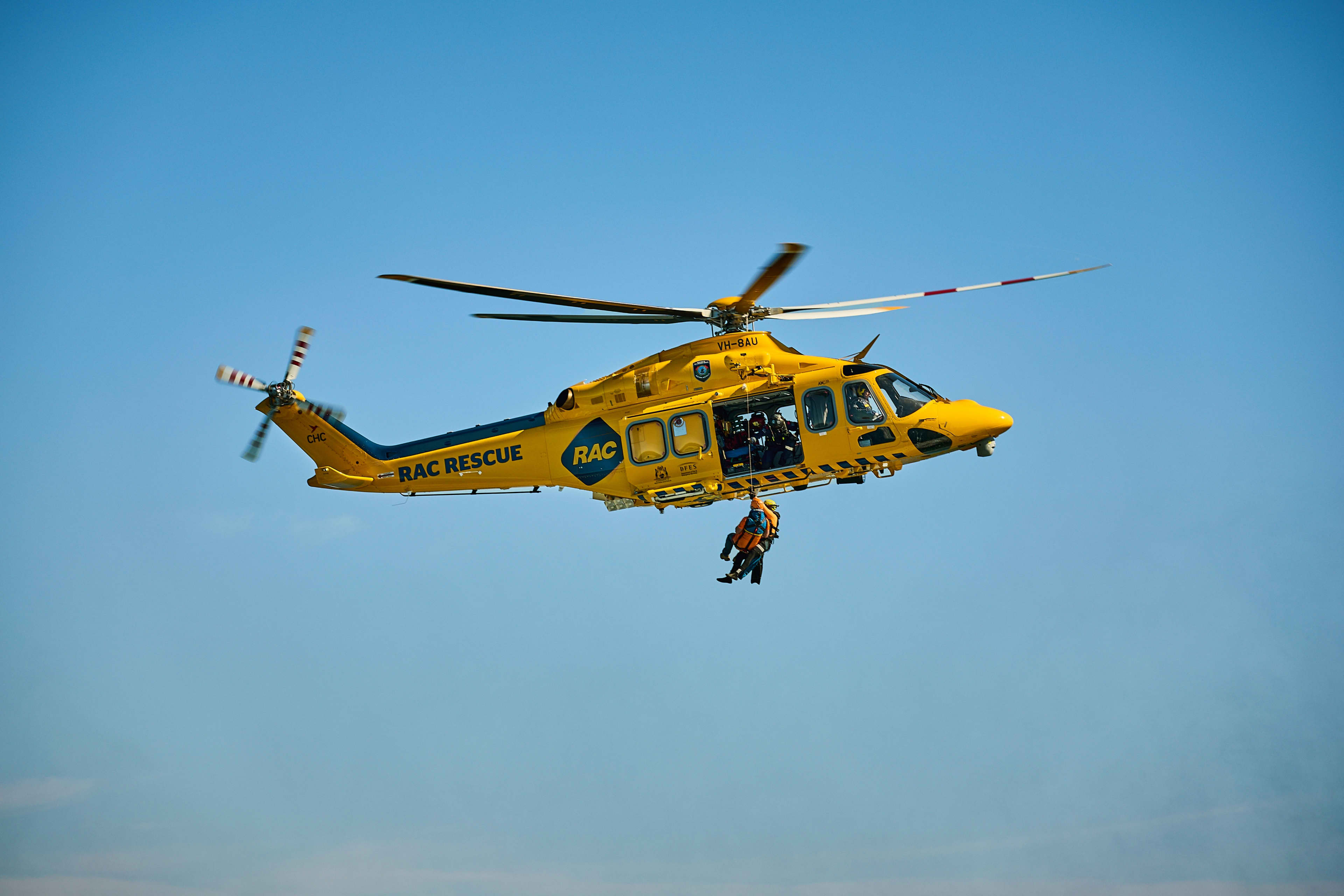 Yellow rescue helicopter flying with someone hanging out of the side of the helicopter.