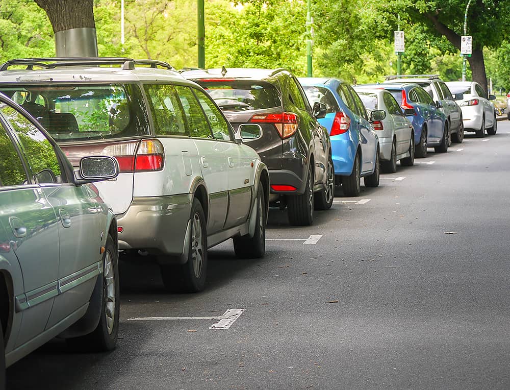 A leafy city street with cars parked on the roadside.