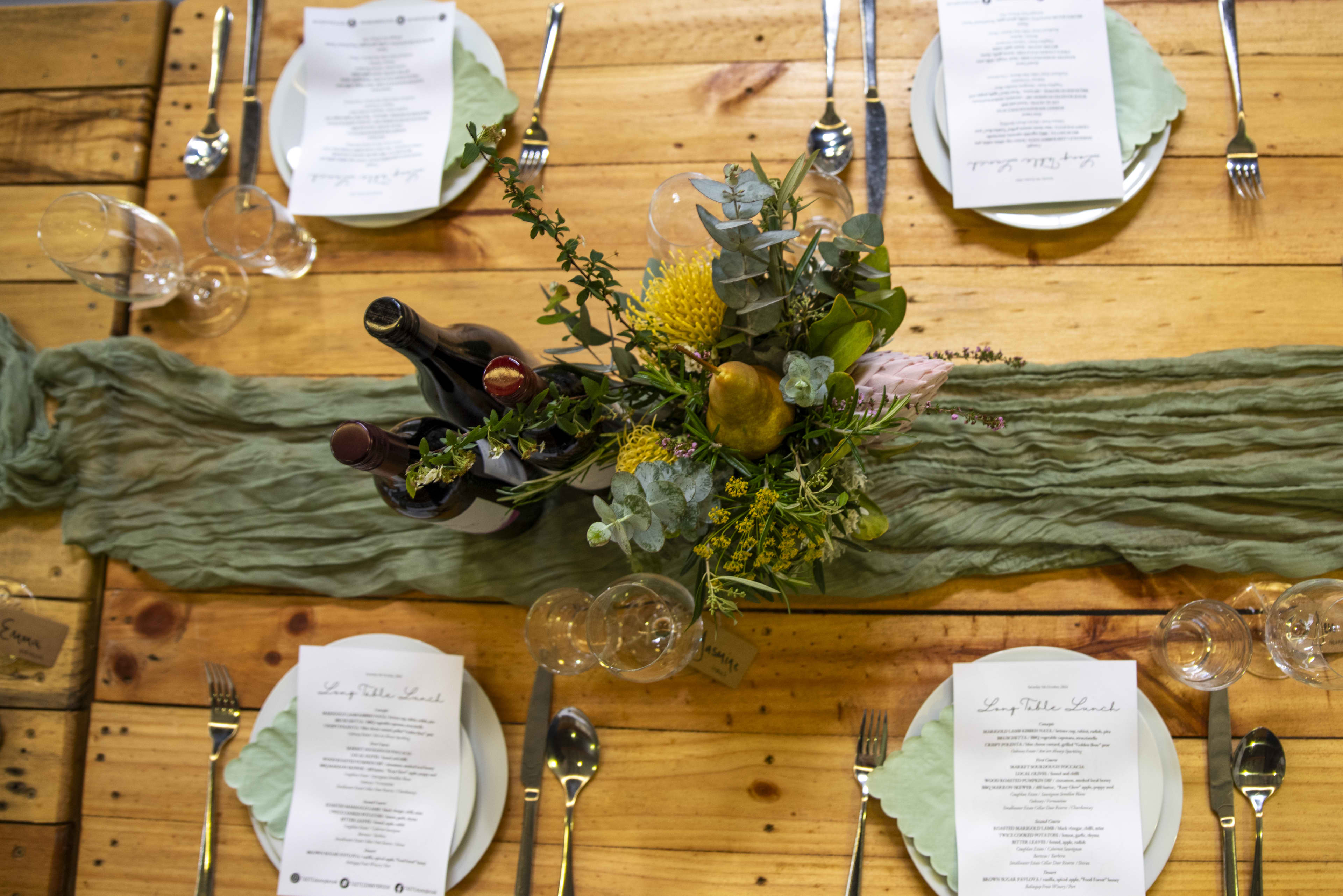Crockery, cutlery and glassware on table with bottles of wine and floral table settings.