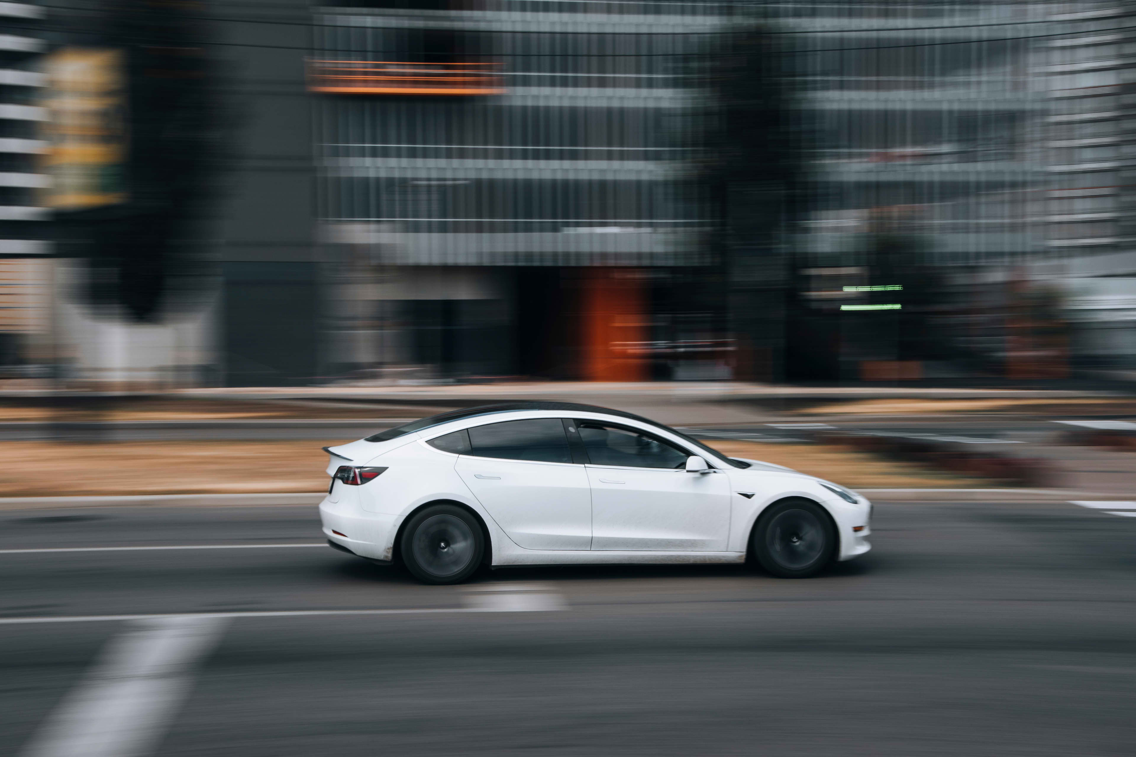 A white Tesla Model 3 driving on a city street.