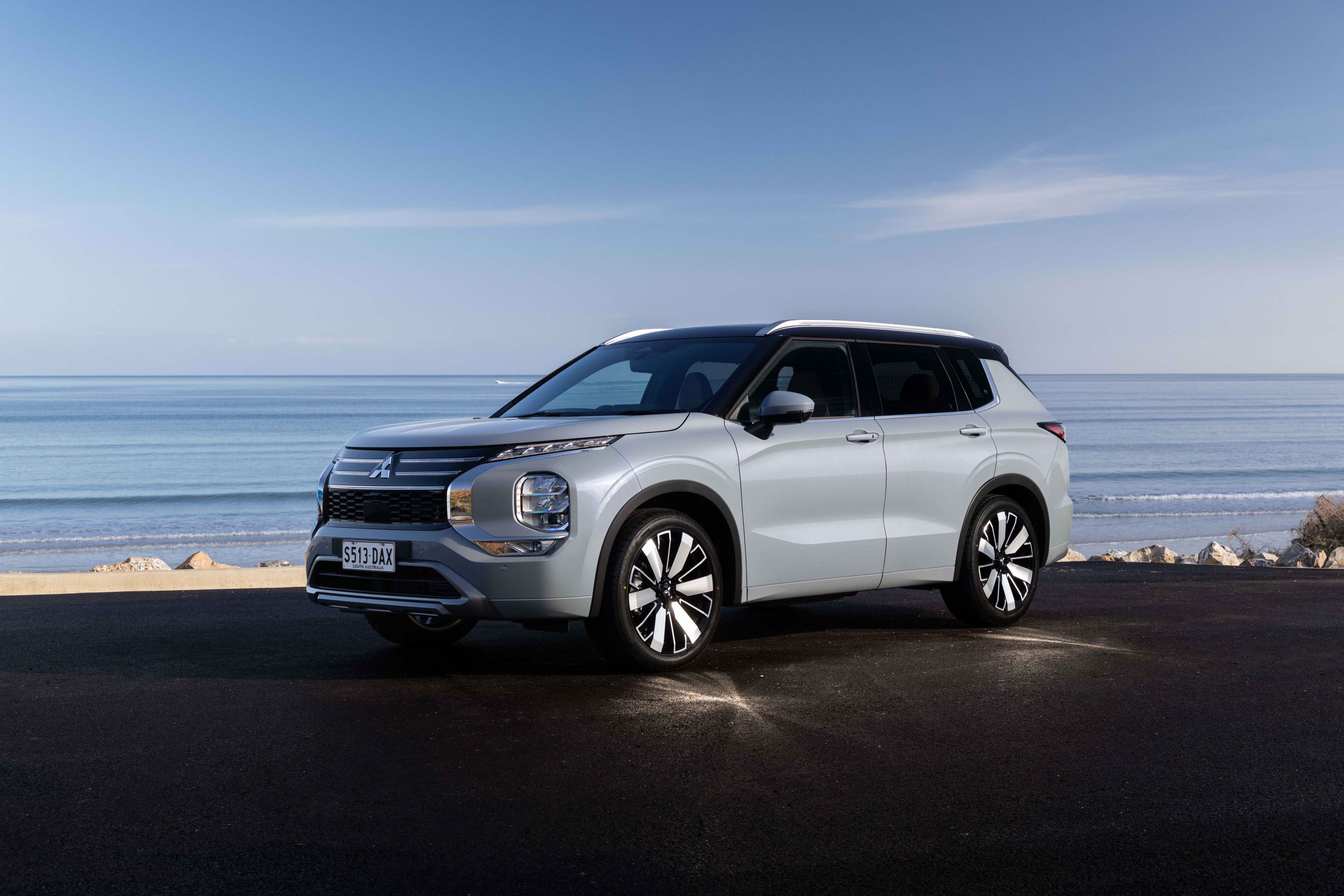 A white Mitsubishi Outlander PHEV parked near a beach