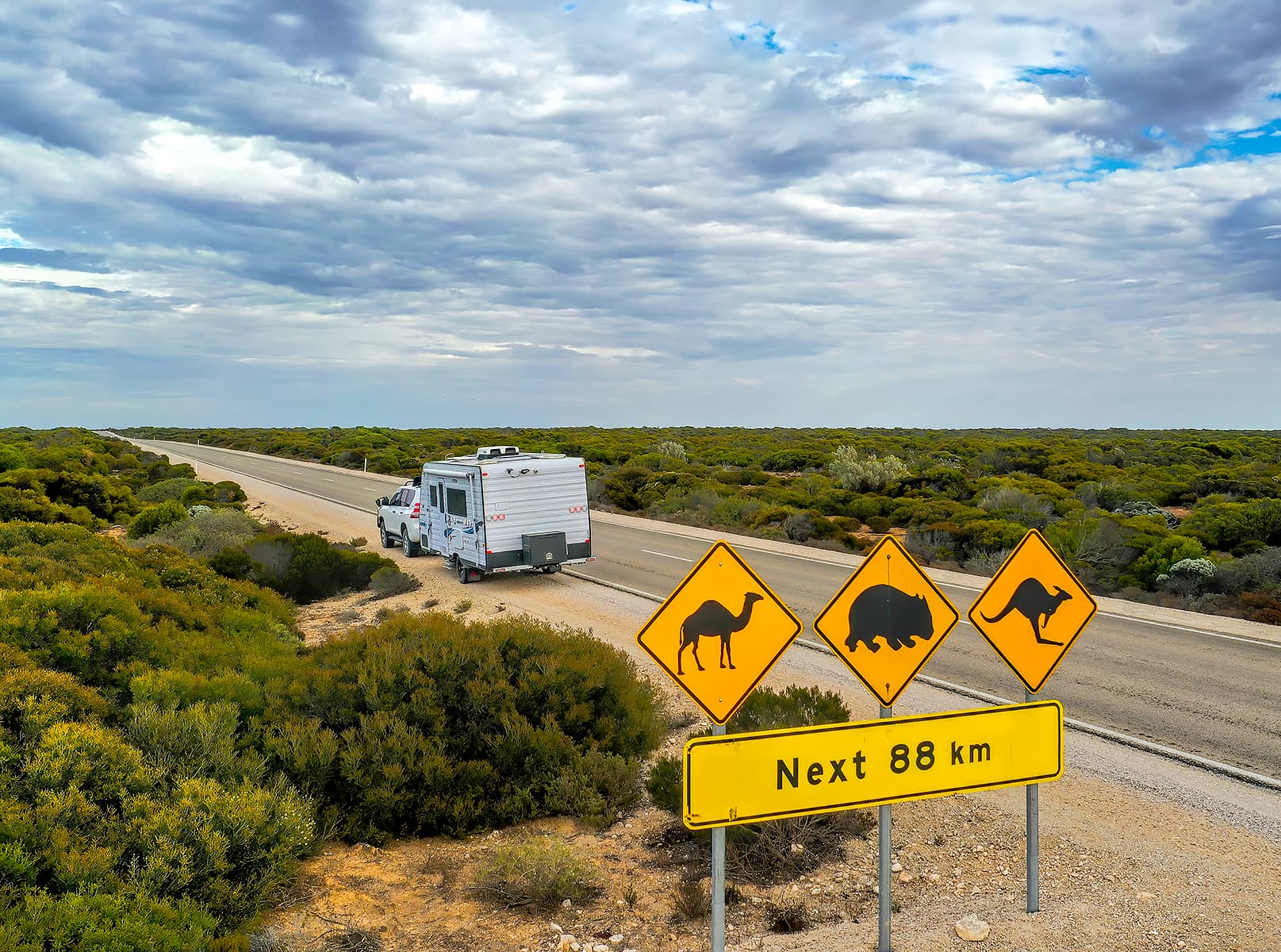A caravan on a remote regional road in Australia passing a wildlife caution sign