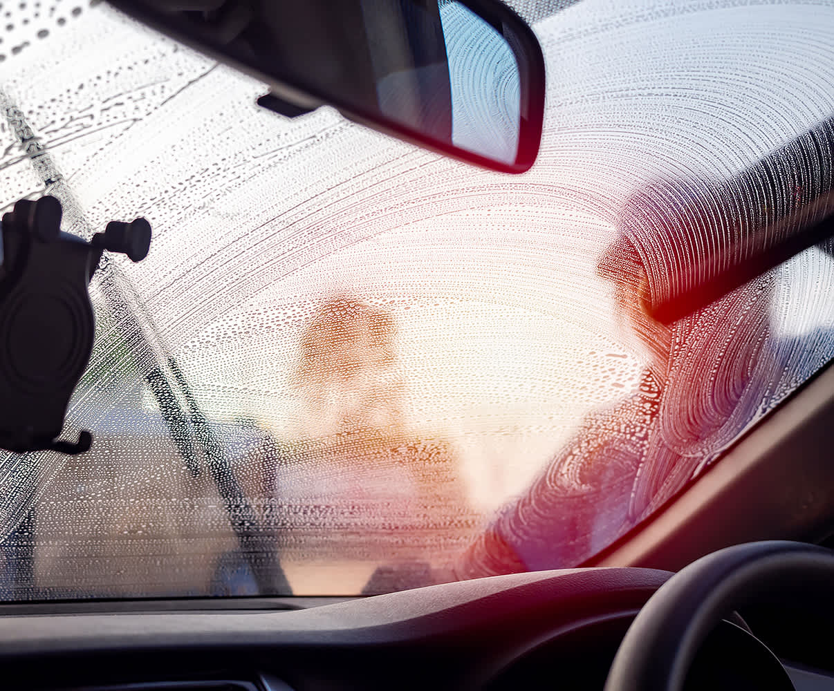 A person washing a windscreen seen from inside the car