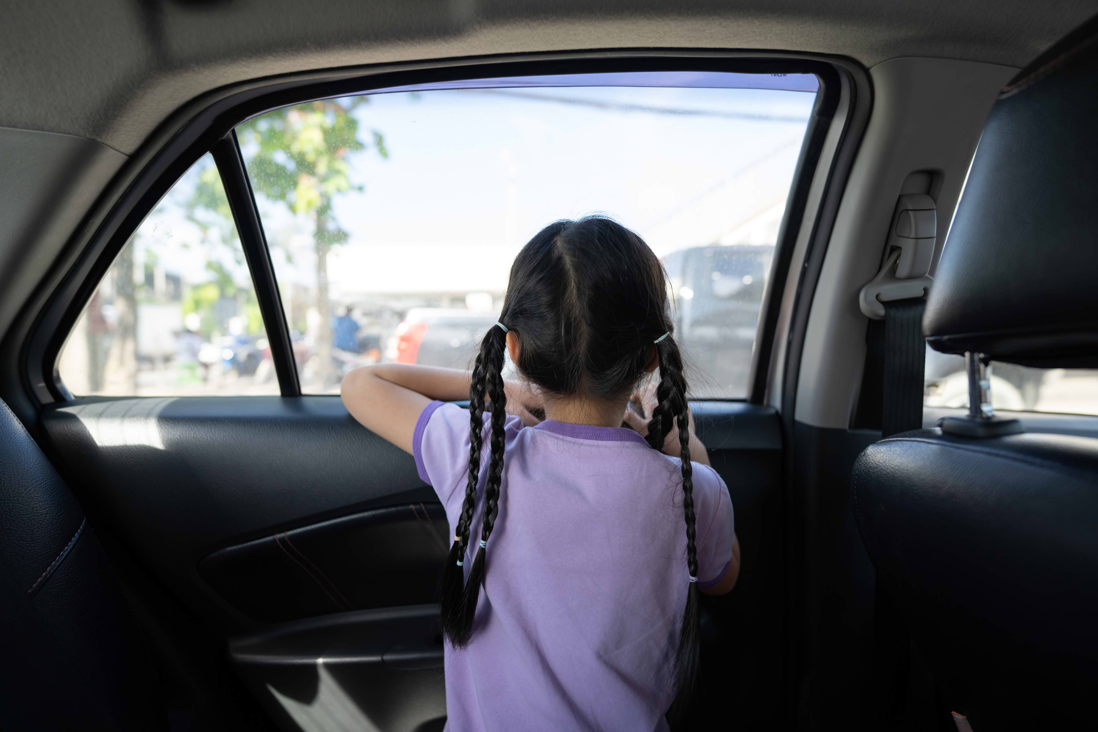 A child looking out through a rear passenger window of a car.
