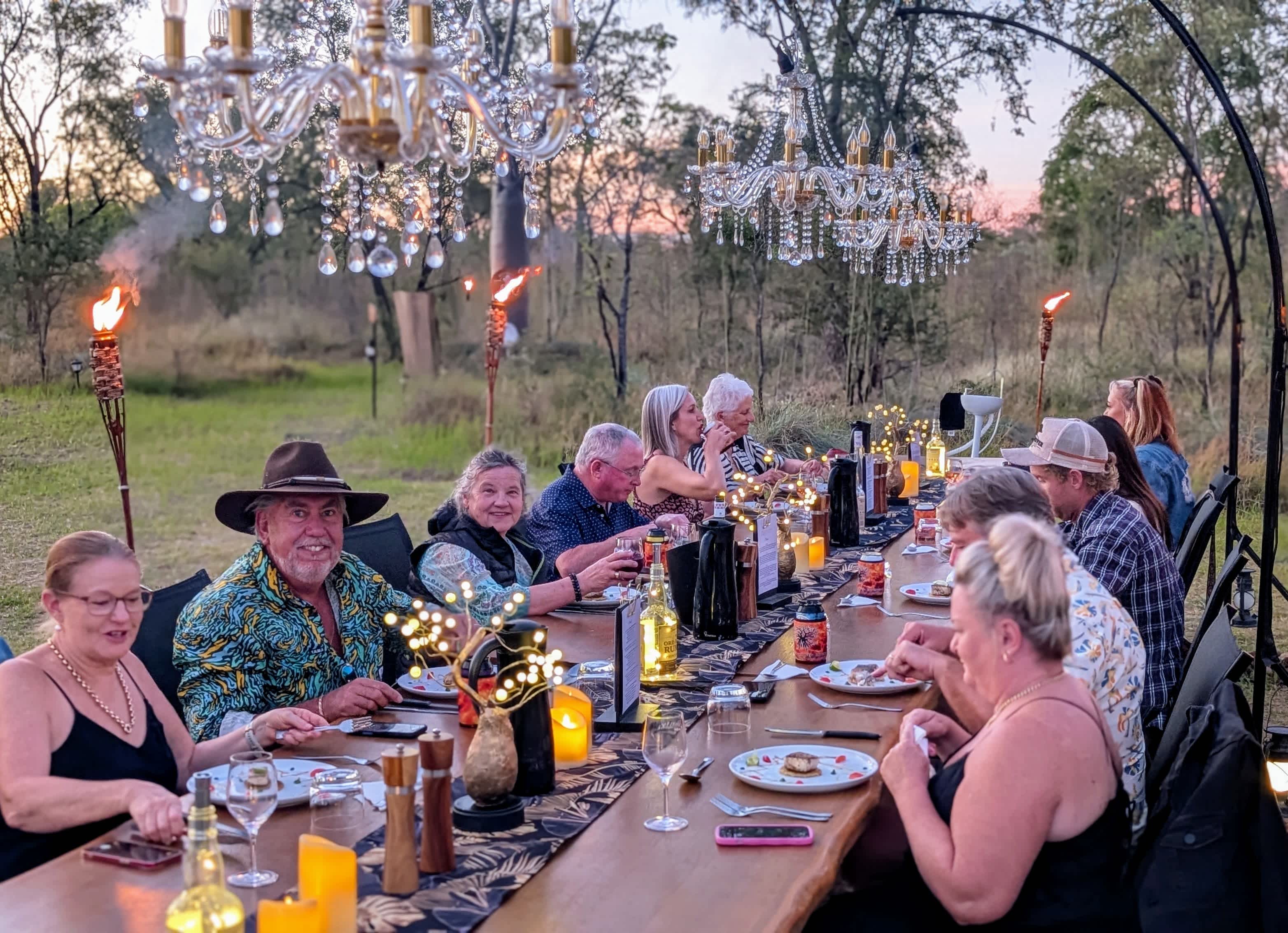 Long Table dining in Kununurra with low hanging chandeliers, and guests enjoying their meals.