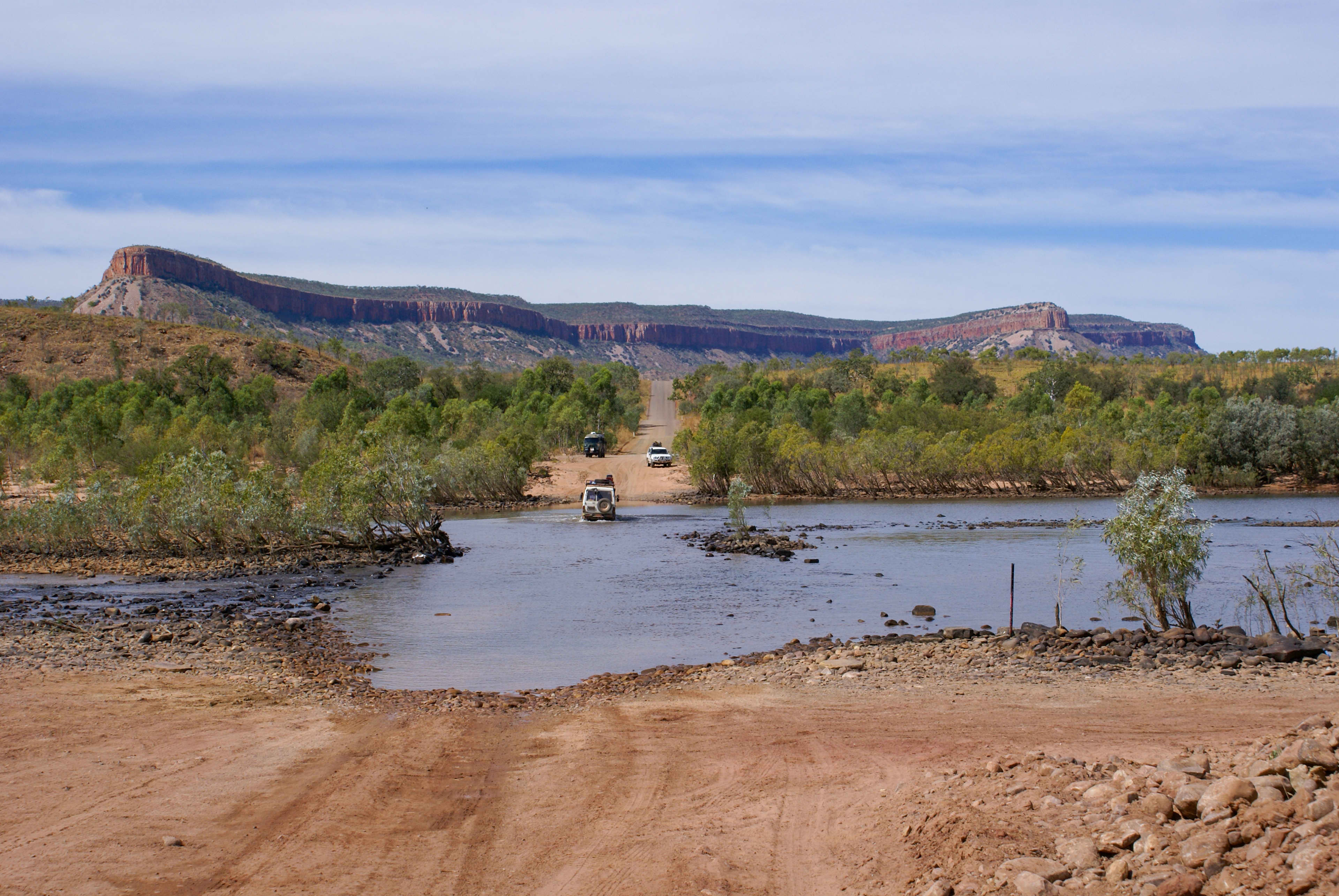 Two four-wheel drive vehicles crossing a river in the WA outbak.