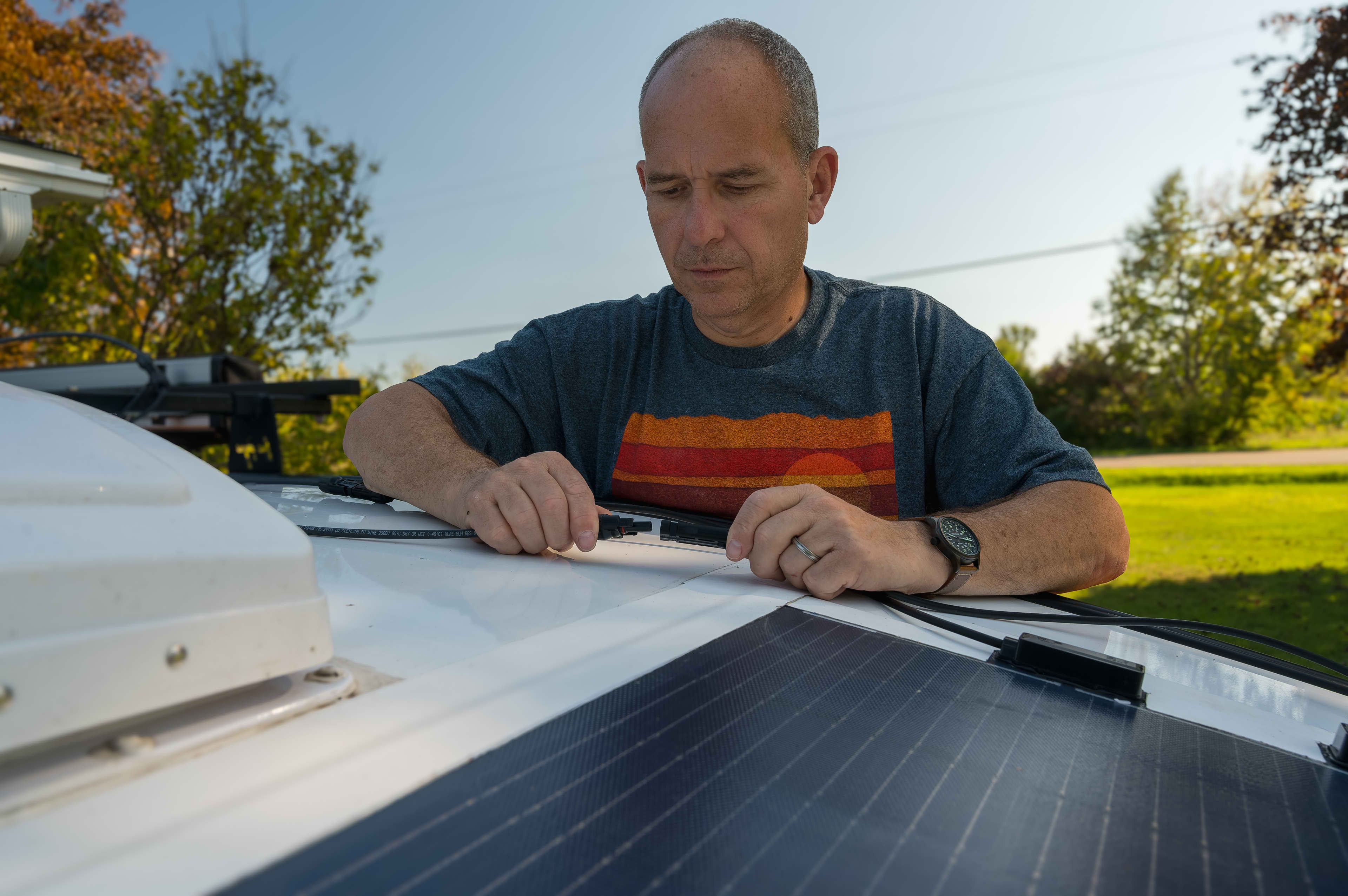 A person is connecting some wiring from solar panels on a caravan roof.