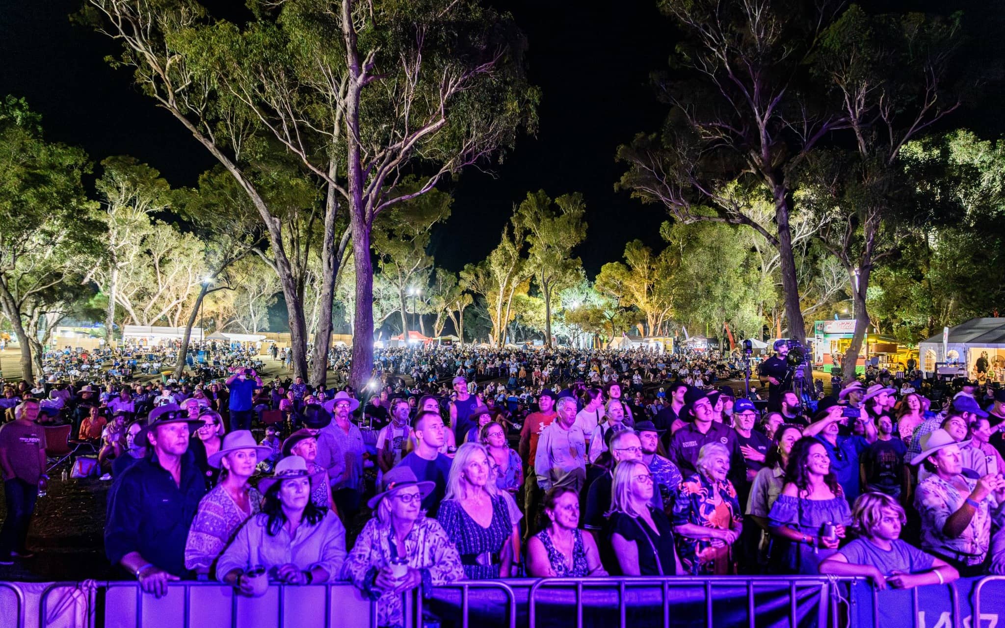 A crowd standing and facing a main stage with purple lighting illuminating them.