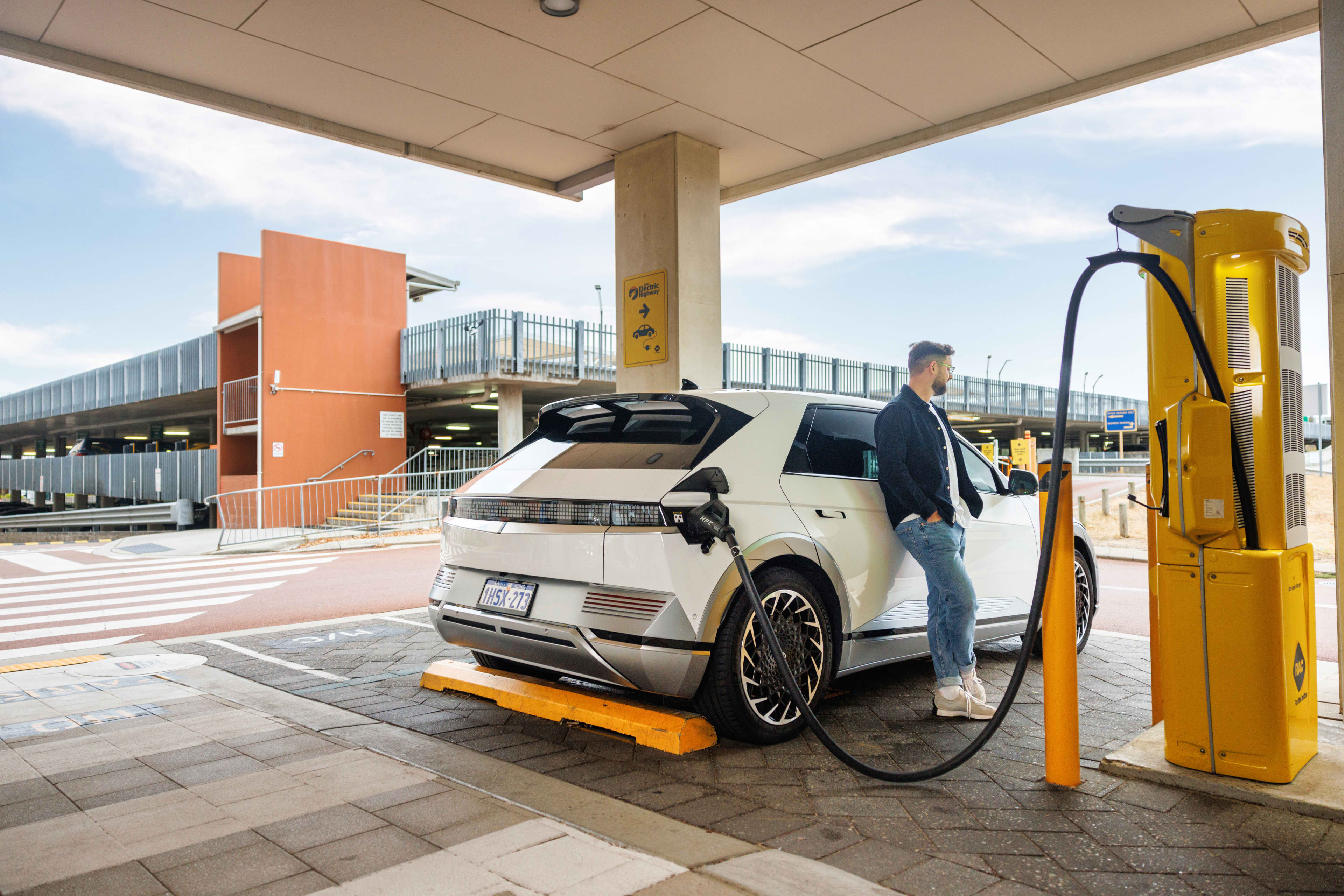 EV owner leaning against electric vehicle while it is charging