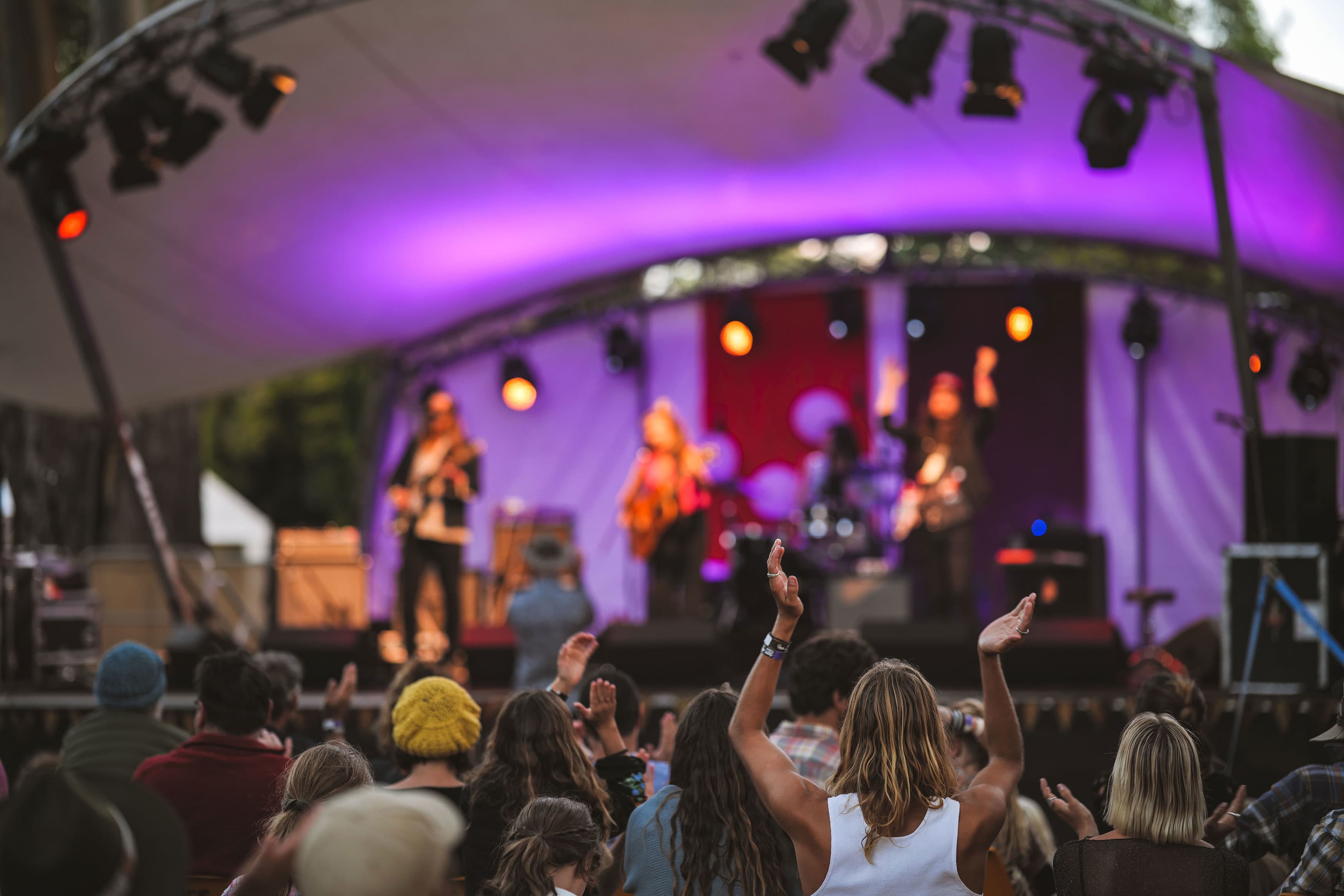 A purple stage in the background with live band, with crowd facing in the foreground