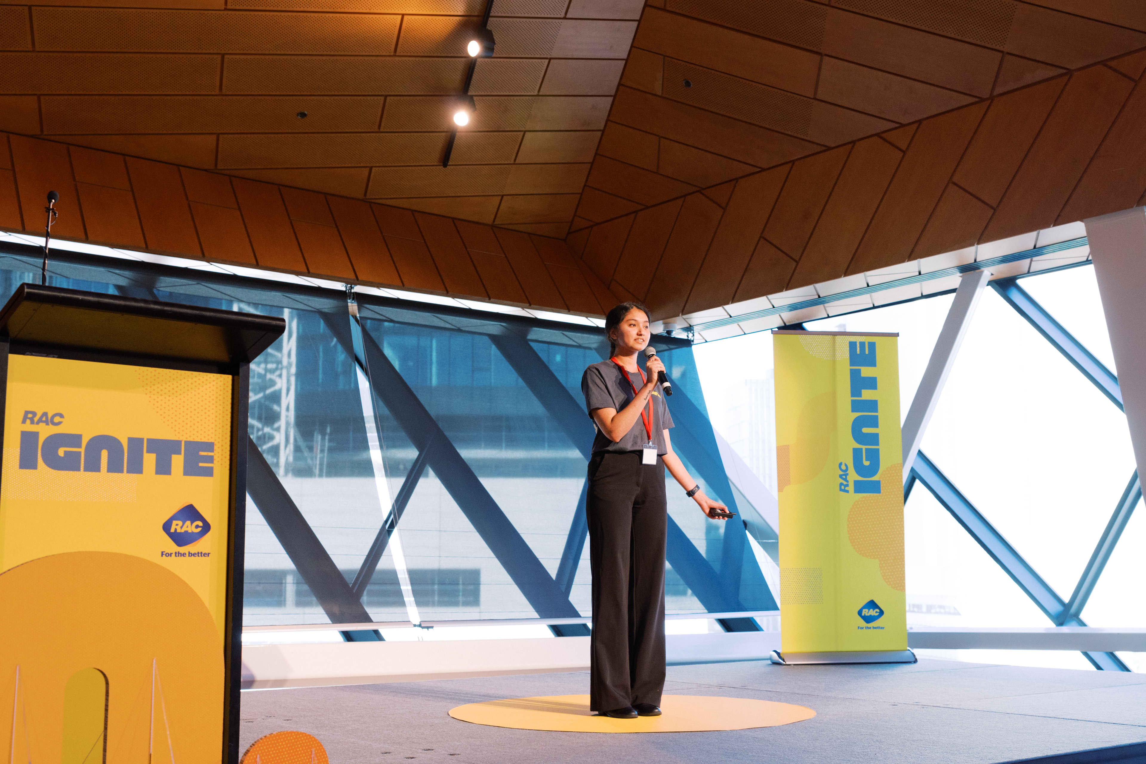 Ignite Leadership Program winner, Chandini, stands on stage with a lectern and bright lights presenting to an audience.