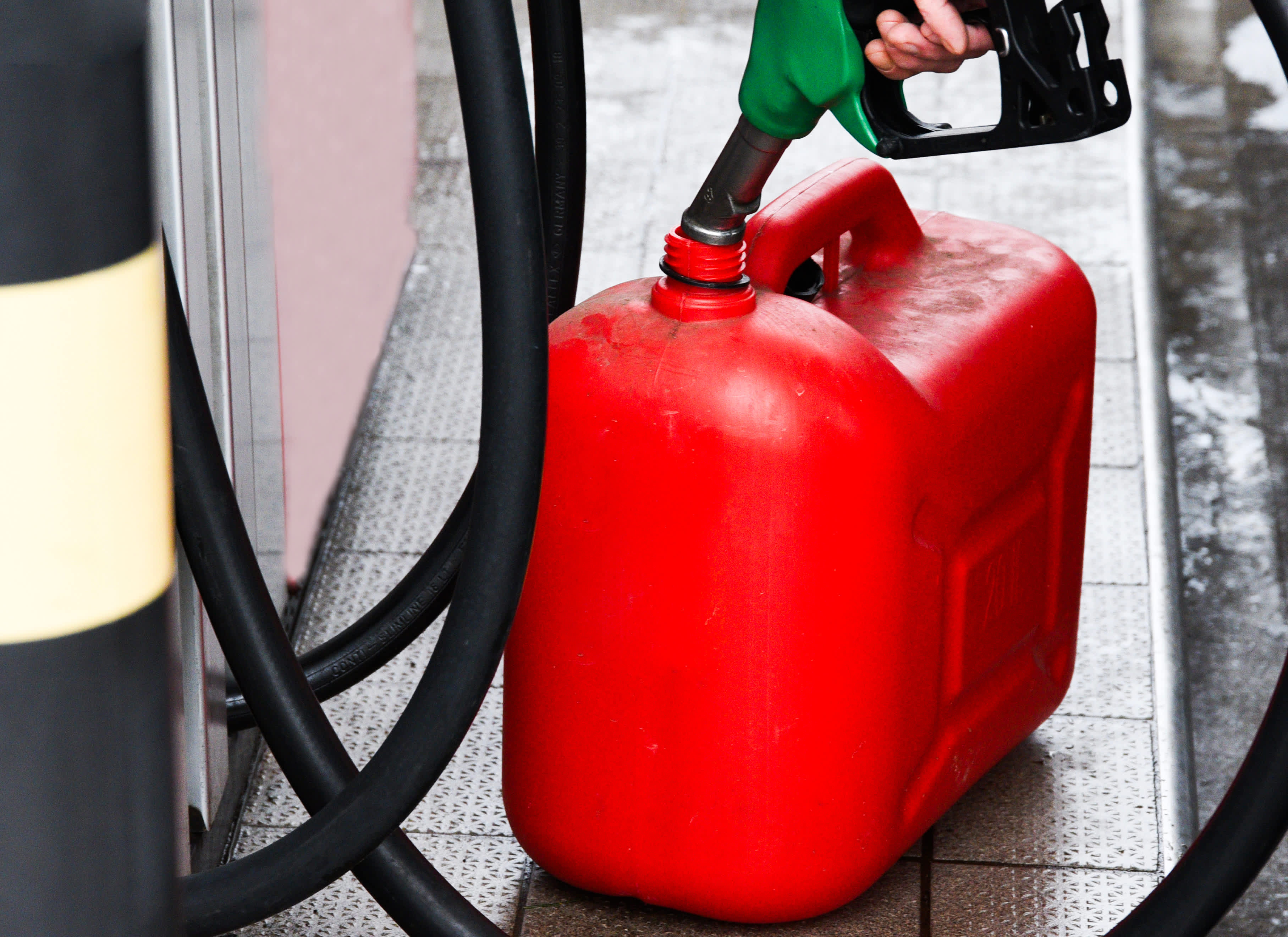 A person filling a red fuel container sitting on the ground near a fuel pump