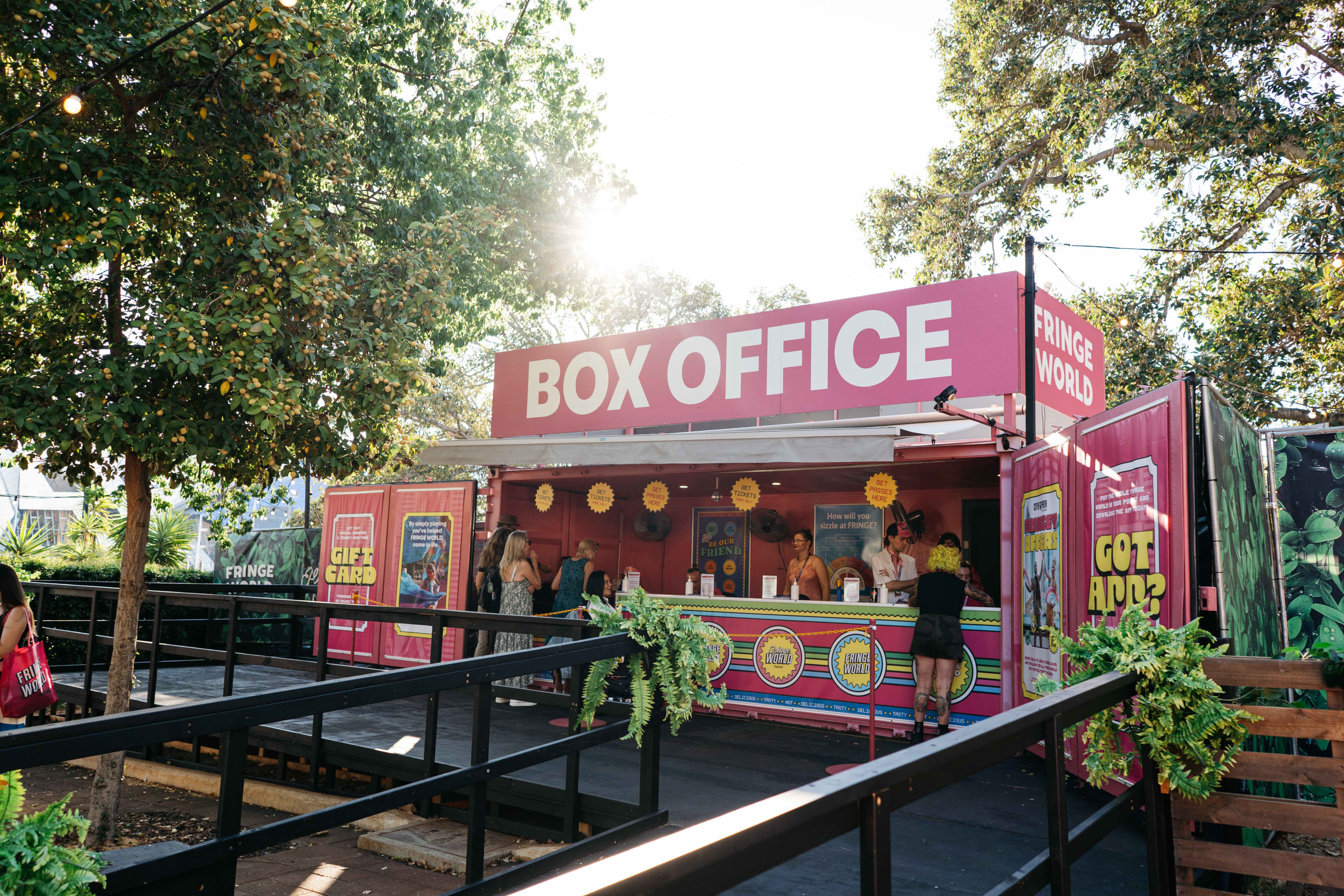 A vibrant pink box office booth sitting amongst lush trees.