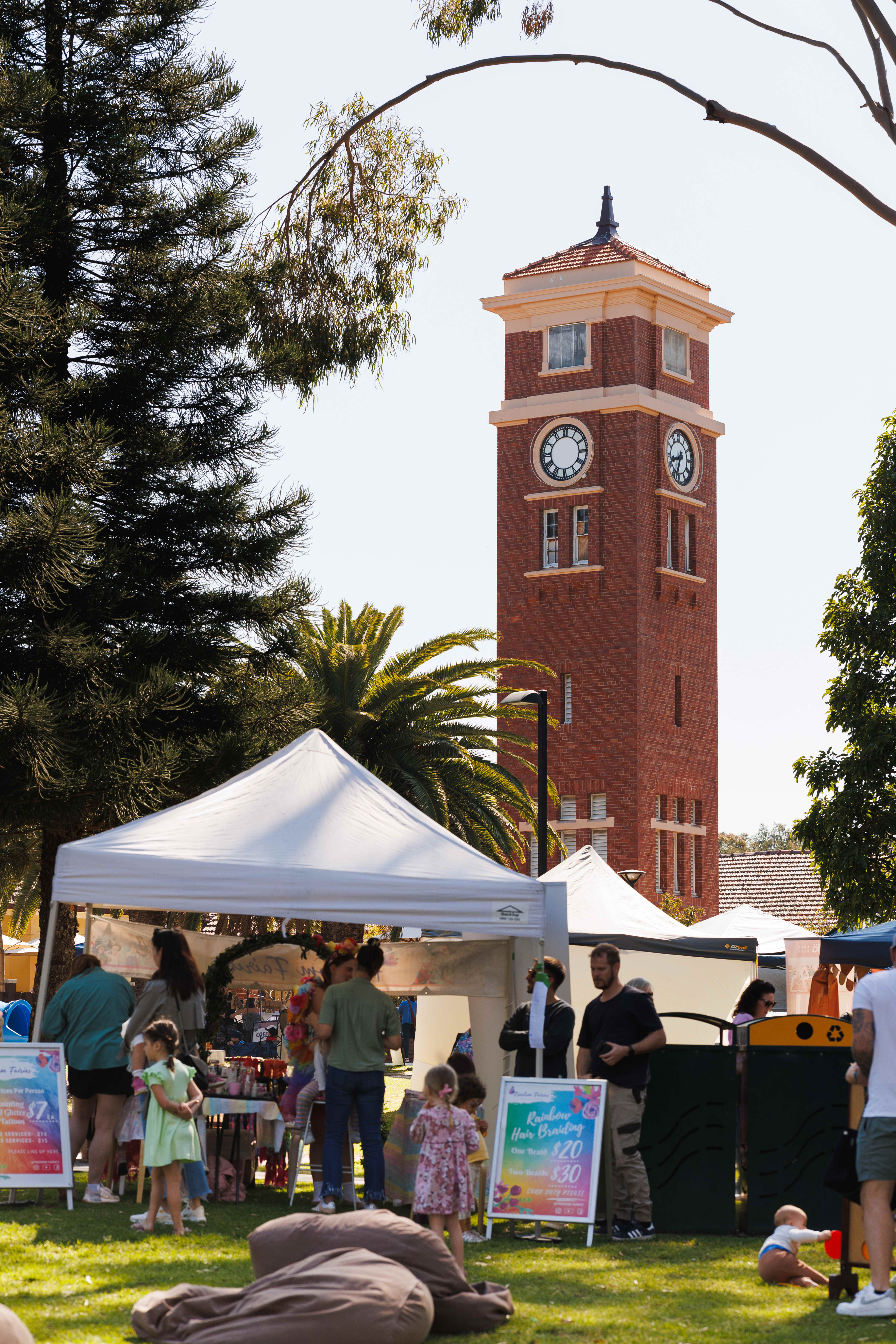 Market stalls in front of old tower surrounded by trees
