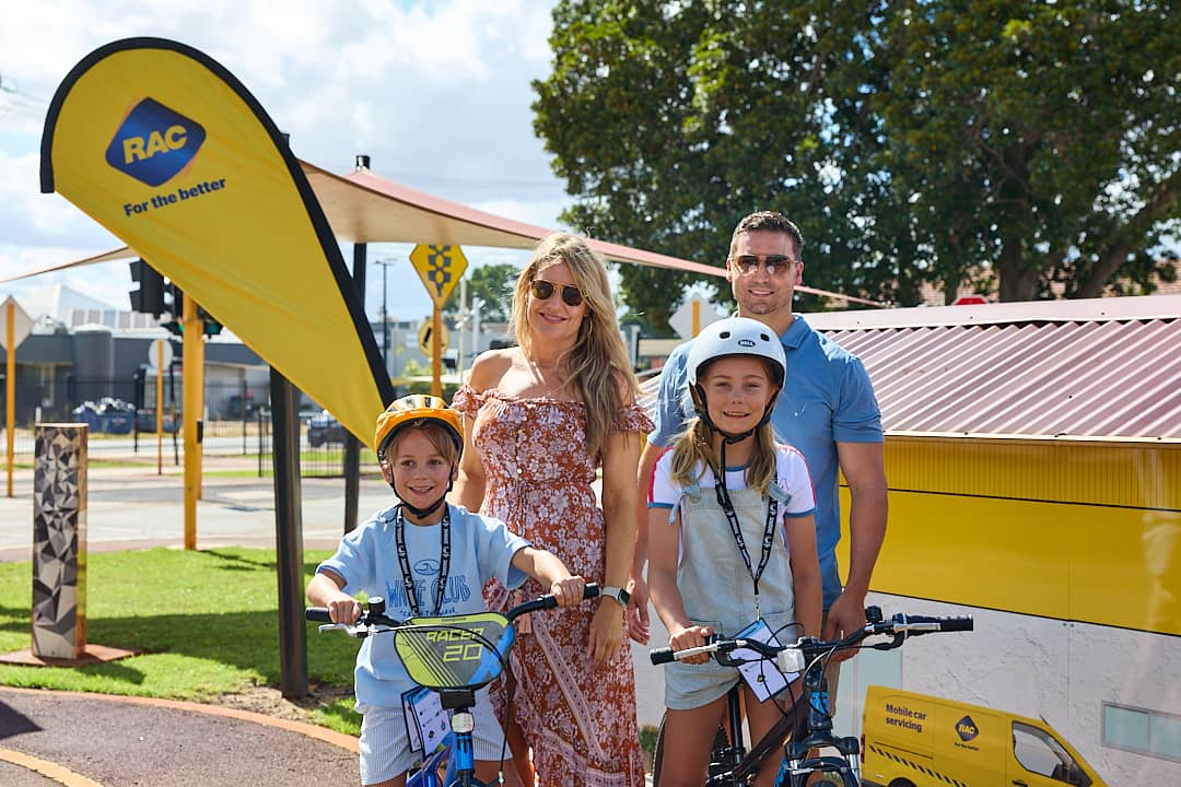 Mother and Father standing behind a young boy and young girl on bikes with helmet's on.