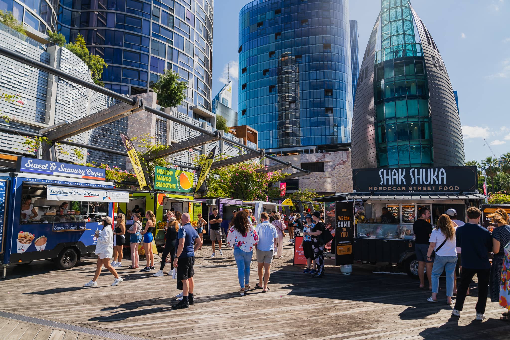 A boardwalk with people wandering looking at a line-up of food trucks.
