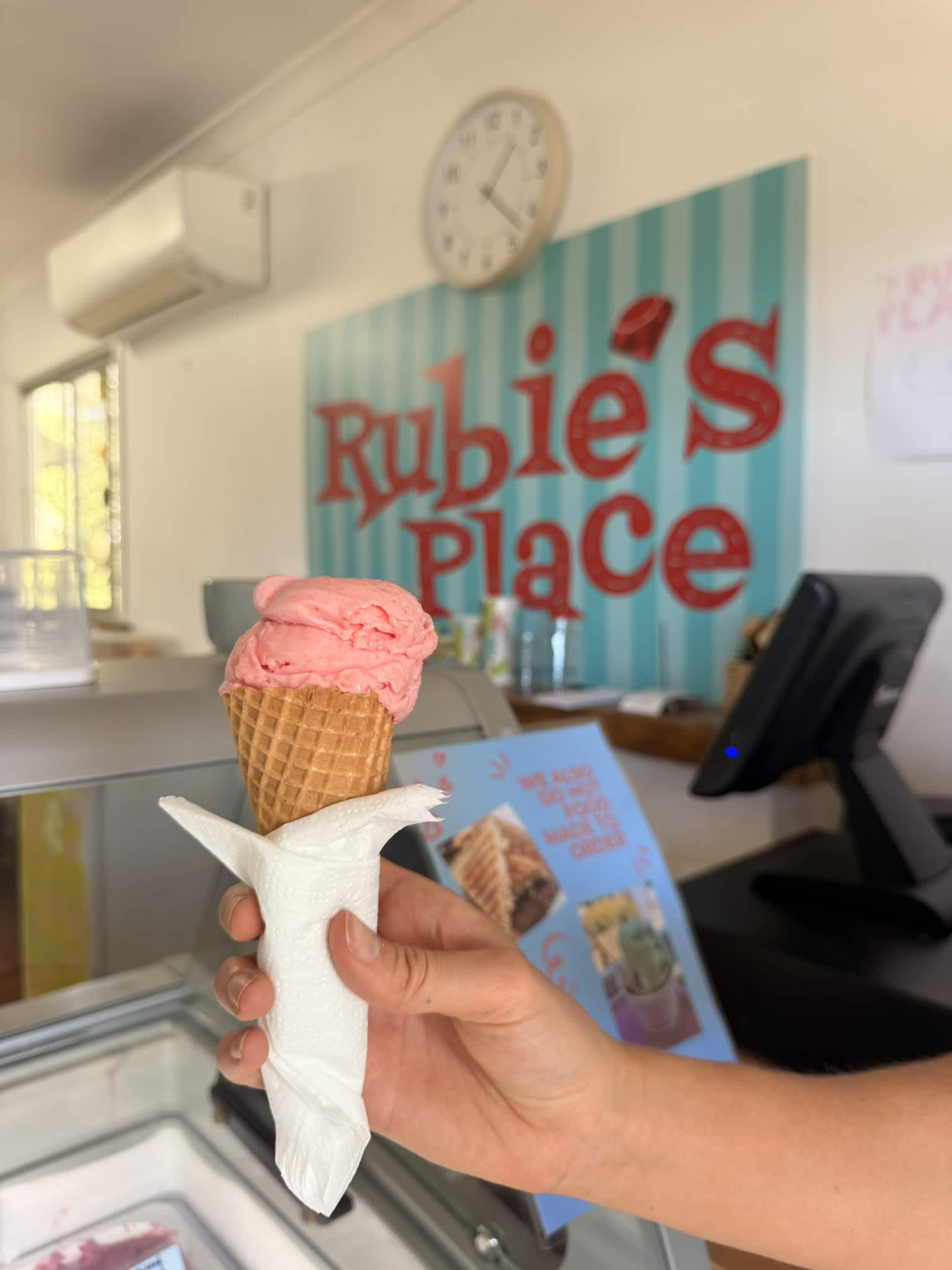 Pink strawberry sorbet in icecream cone in front of colourful icecream cabinet.