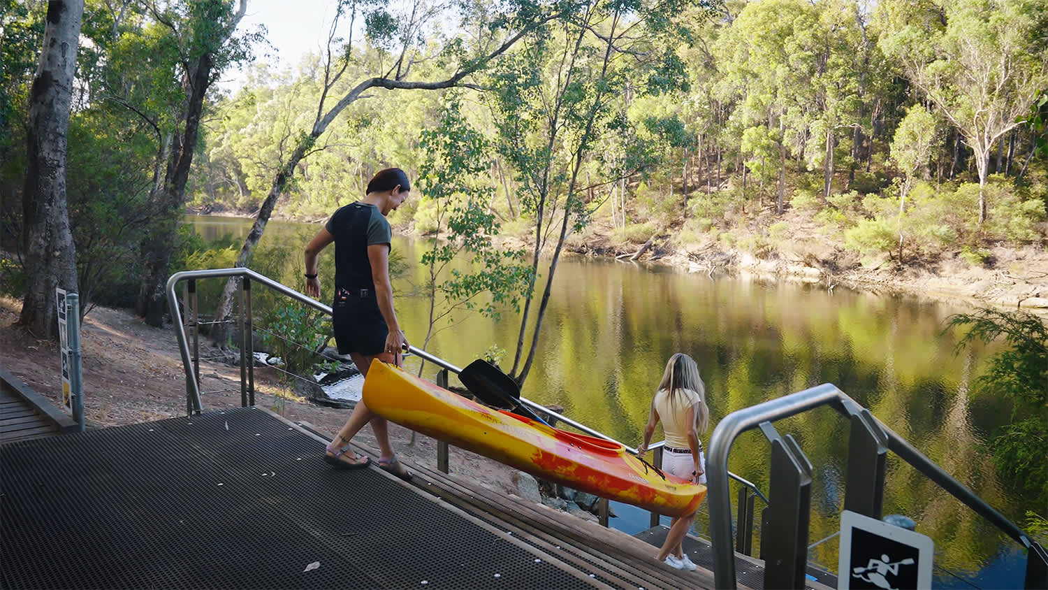 Two people carry a kayak down to a river