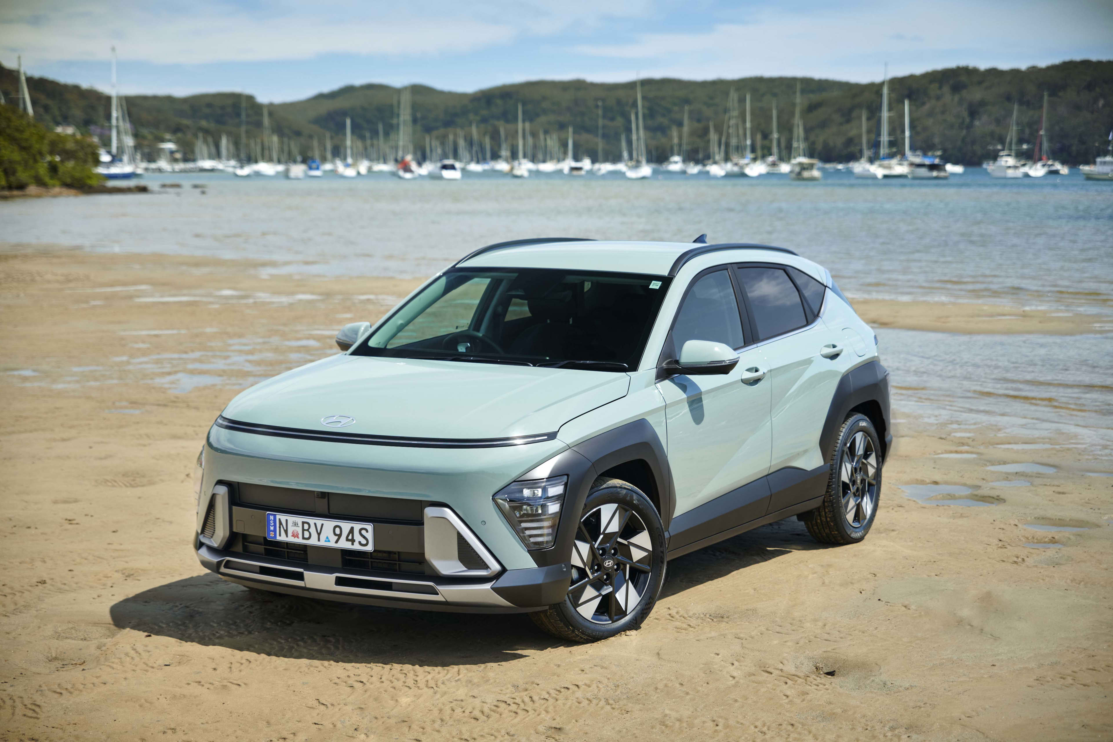 A light green Hyundai Kona hybrid parked on a river shoreline