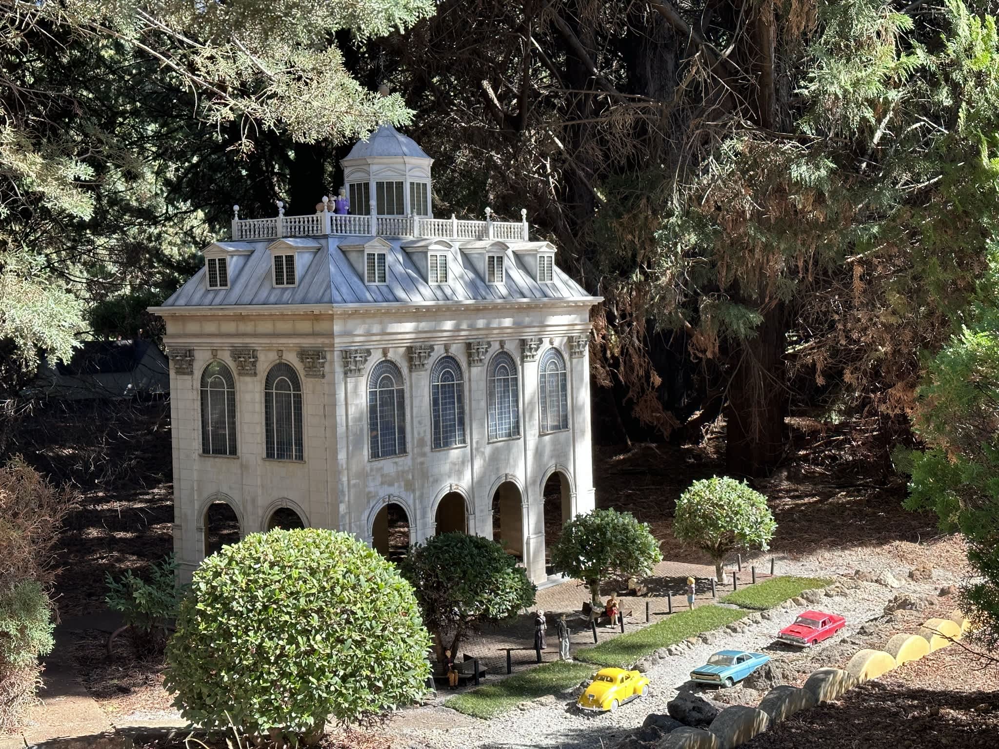Miniature mansion with miniature cars in forest.