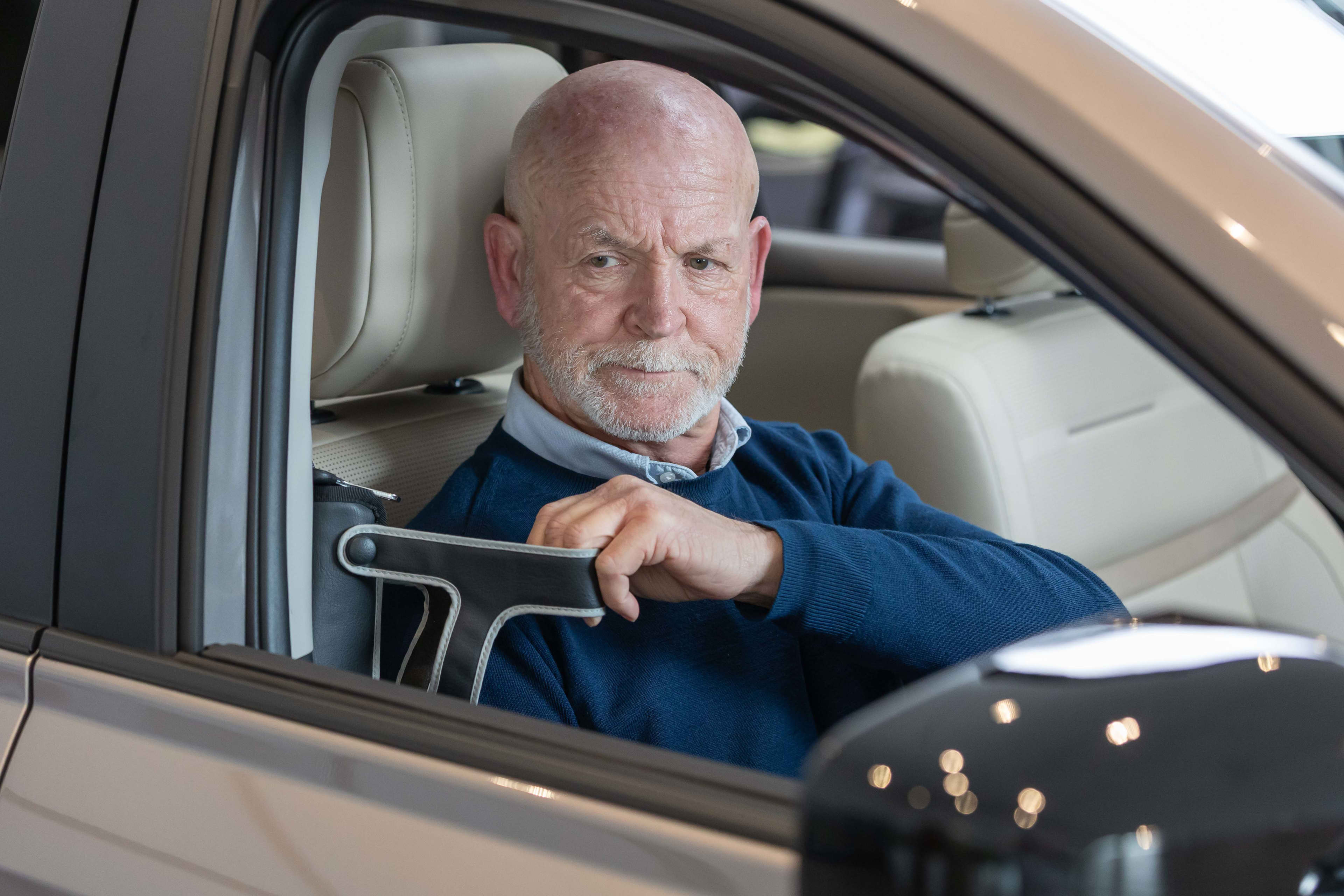 A man seated in a drivers seat of a car pulling on a seatbelt