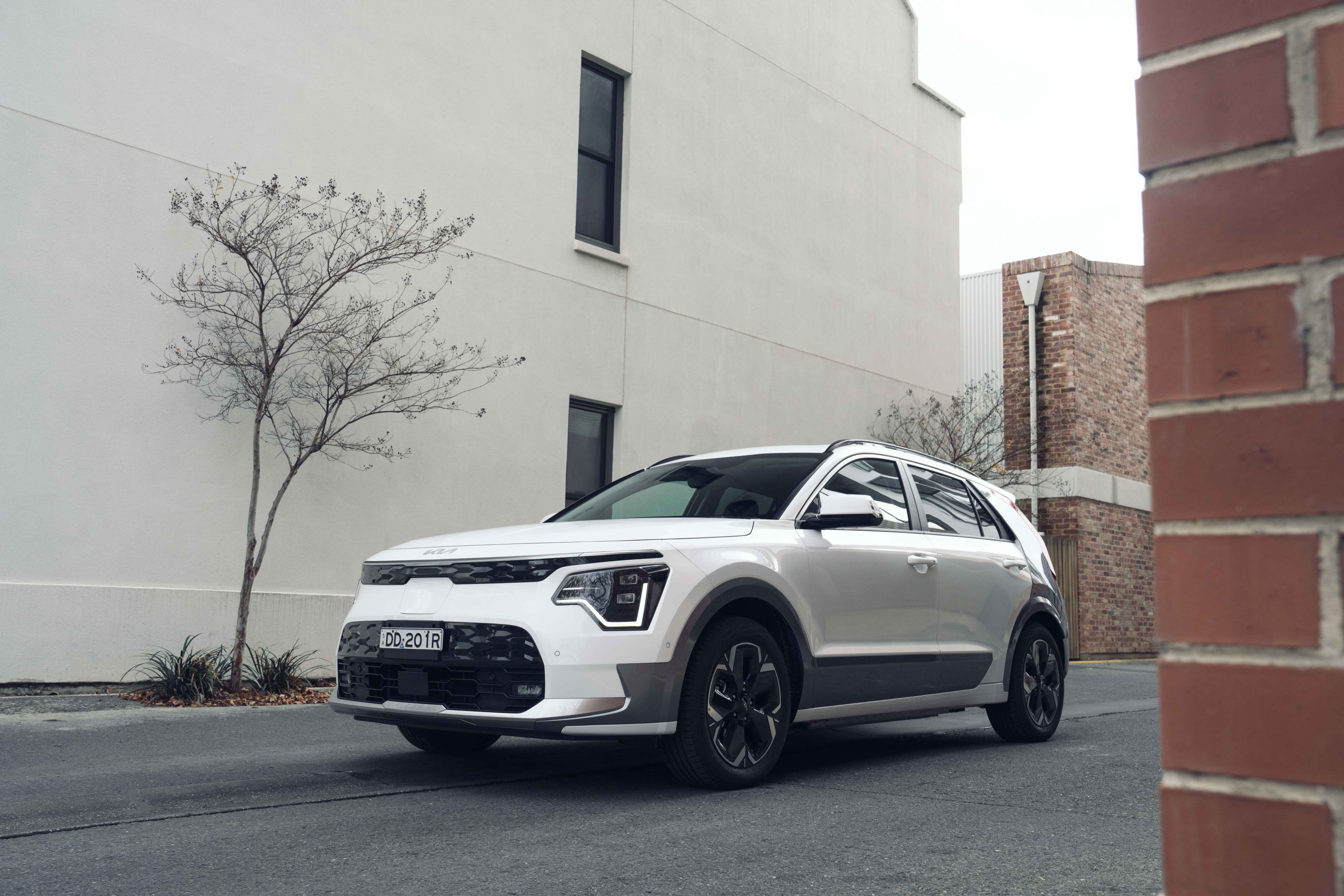 A white Kia Niro EV driving past a building.