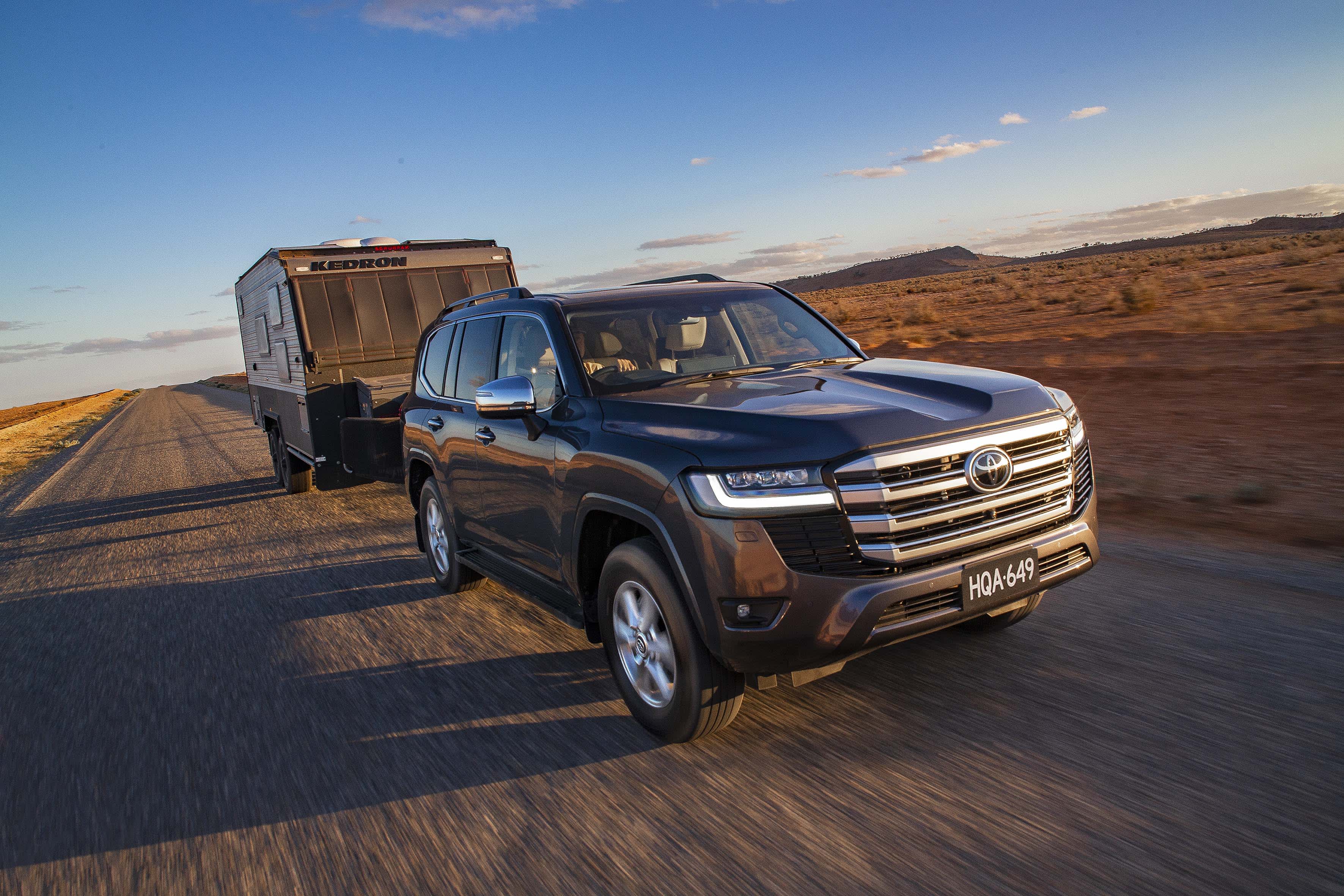 A dark coloured Toyota Landcruiser towing a caravan on a regional road.