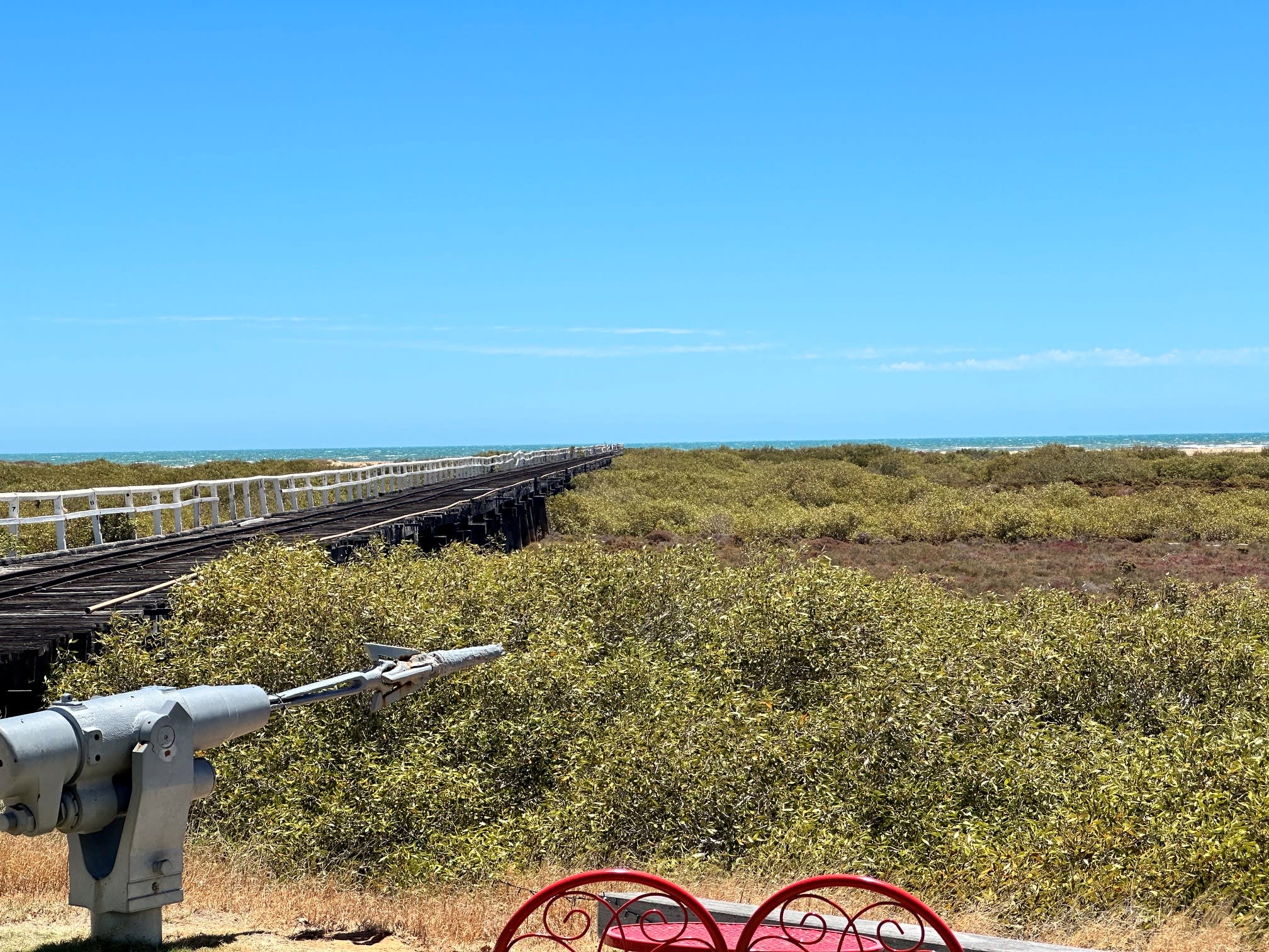 Timber jetty on bushland stretching out to ocean.