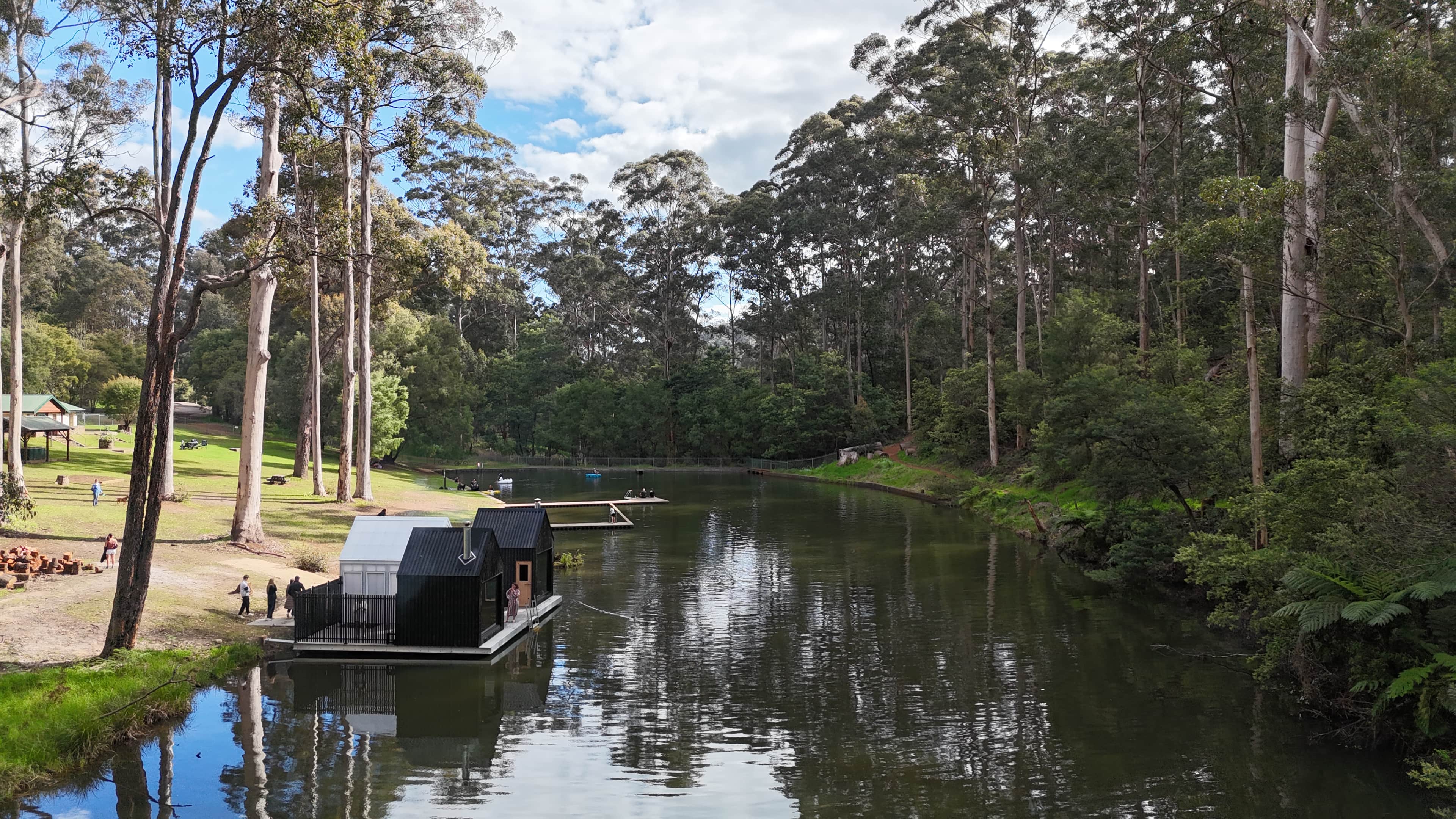 A natural swimming hole surrounded by trees with a small sauna floating by river bank.