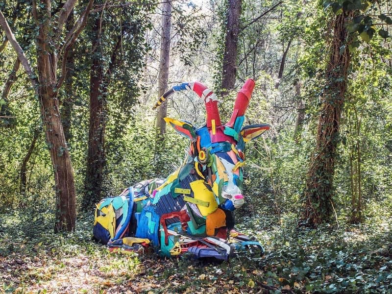 Large colourful goat creature sculpture in forest.