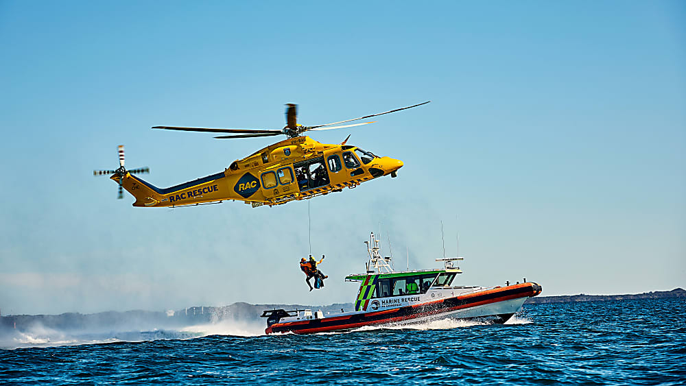 The yellow RAC Helicopter is hoisting two people up from a boat out at sea